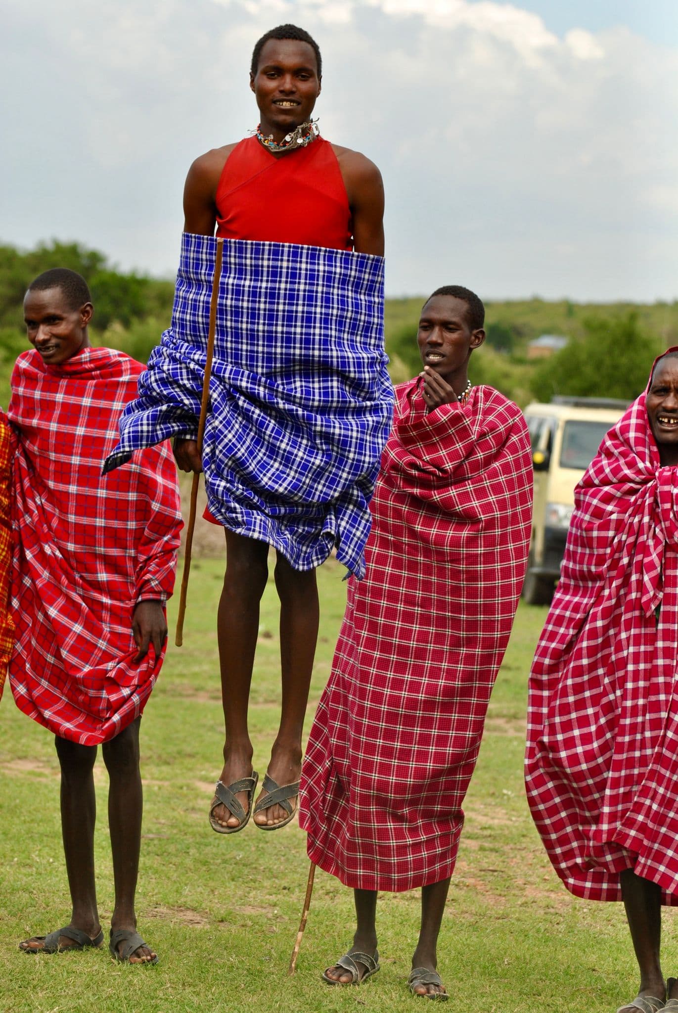 Maasai man mid-jump during a traditional jumping dance, surrounded by others on the Maasai Mara plains, Kenya.