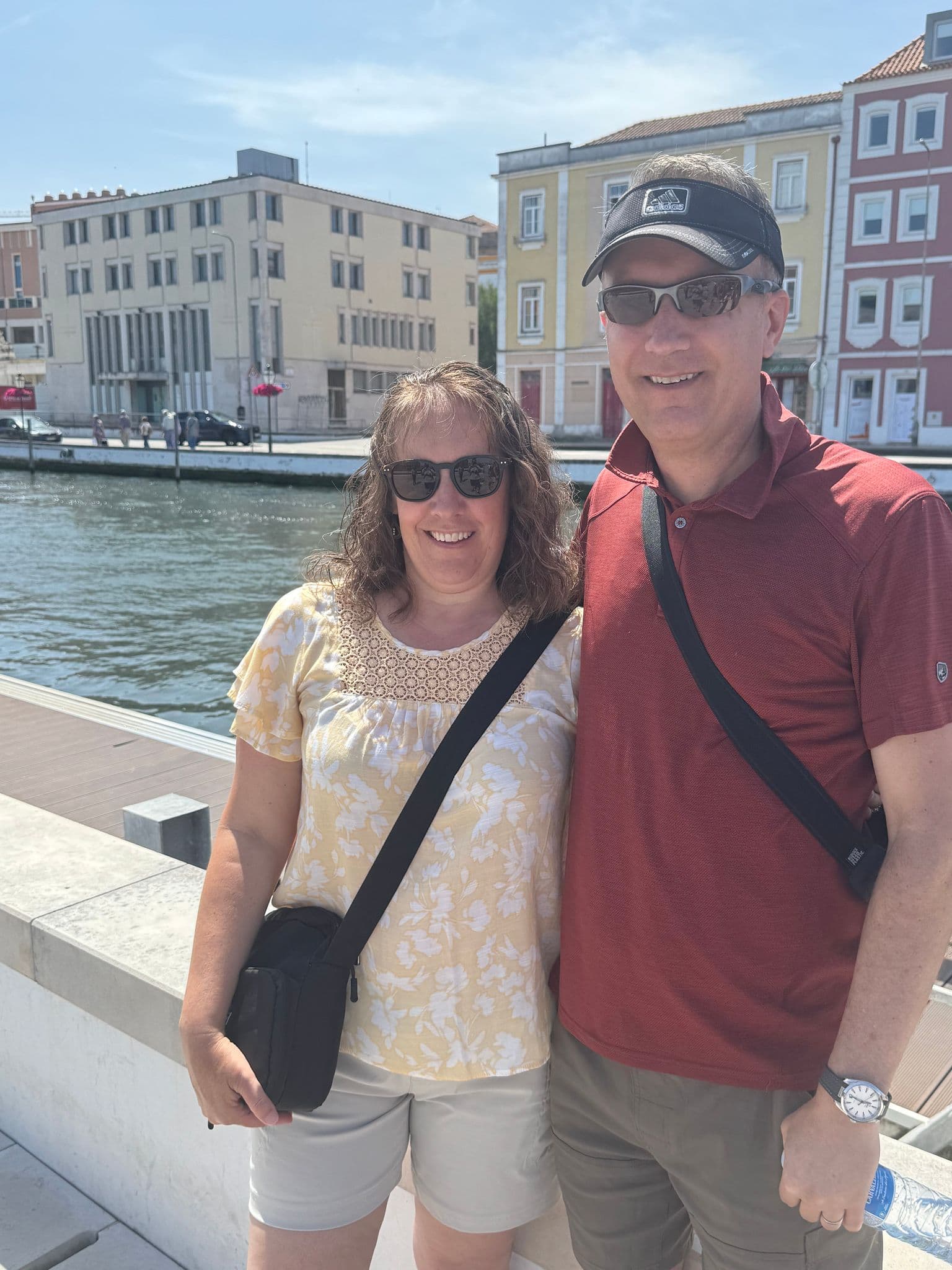 Aveiro canal with two travelers standing at the water's edge and colorful buildings behind them, Aveiro, Portugal.