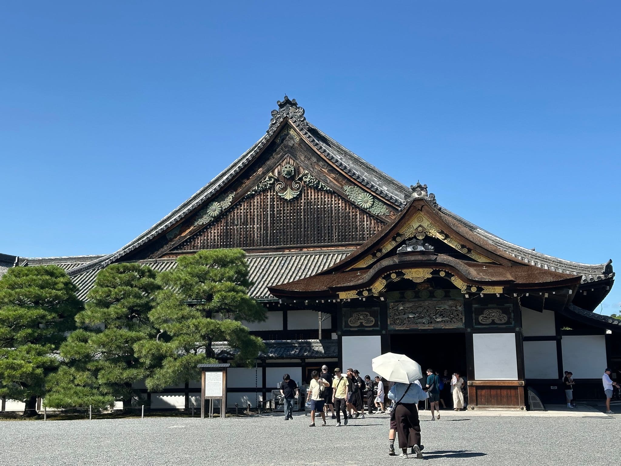 Nijo Castle Ninomaru Palace entrance with tourists walking toward it under a clear blue sky, Kyoto, Japan.