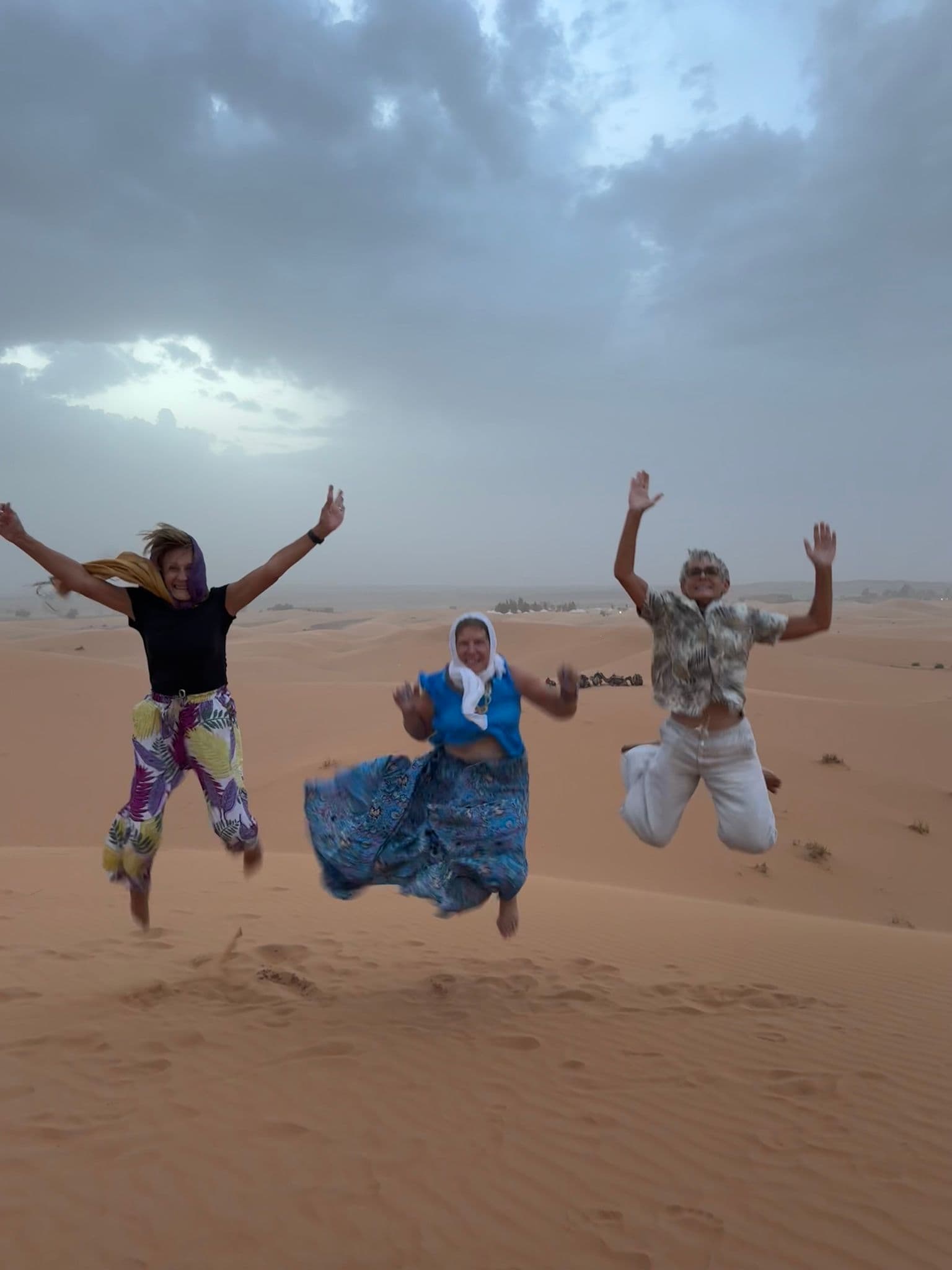 Sahara Desert sand dunes with three travelers jumping above the sand on a trip in Morocco.