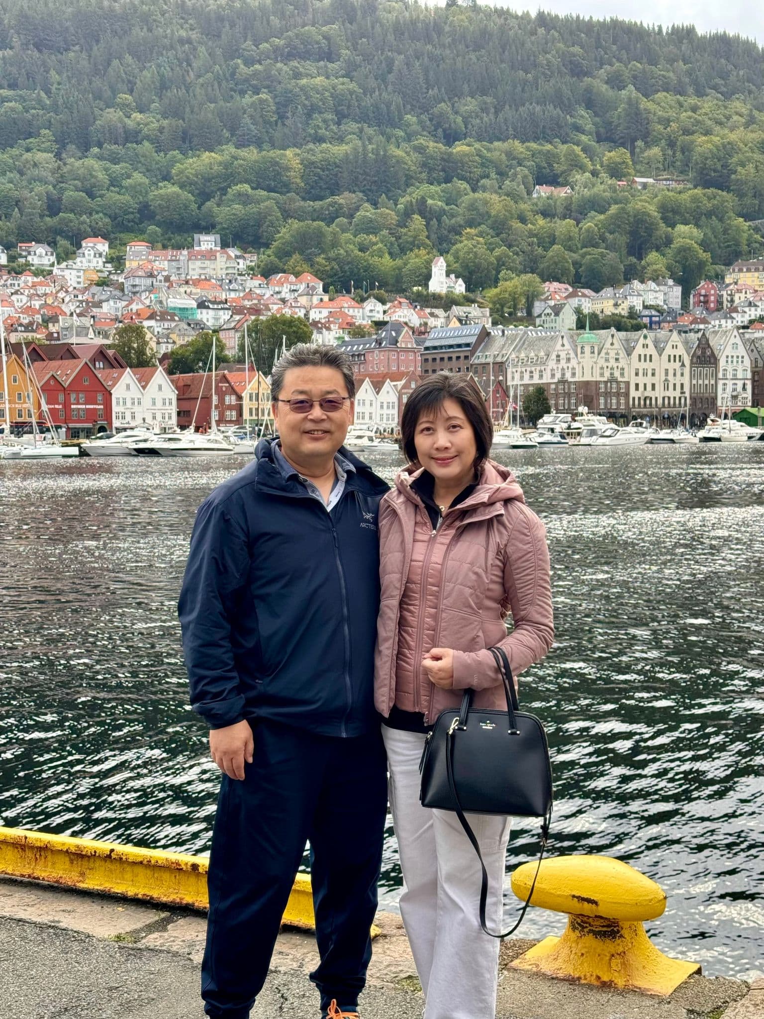 Bryggen wooden waterfront in Bergen, Norway, with a couple posing on the harbor edge during a trip.