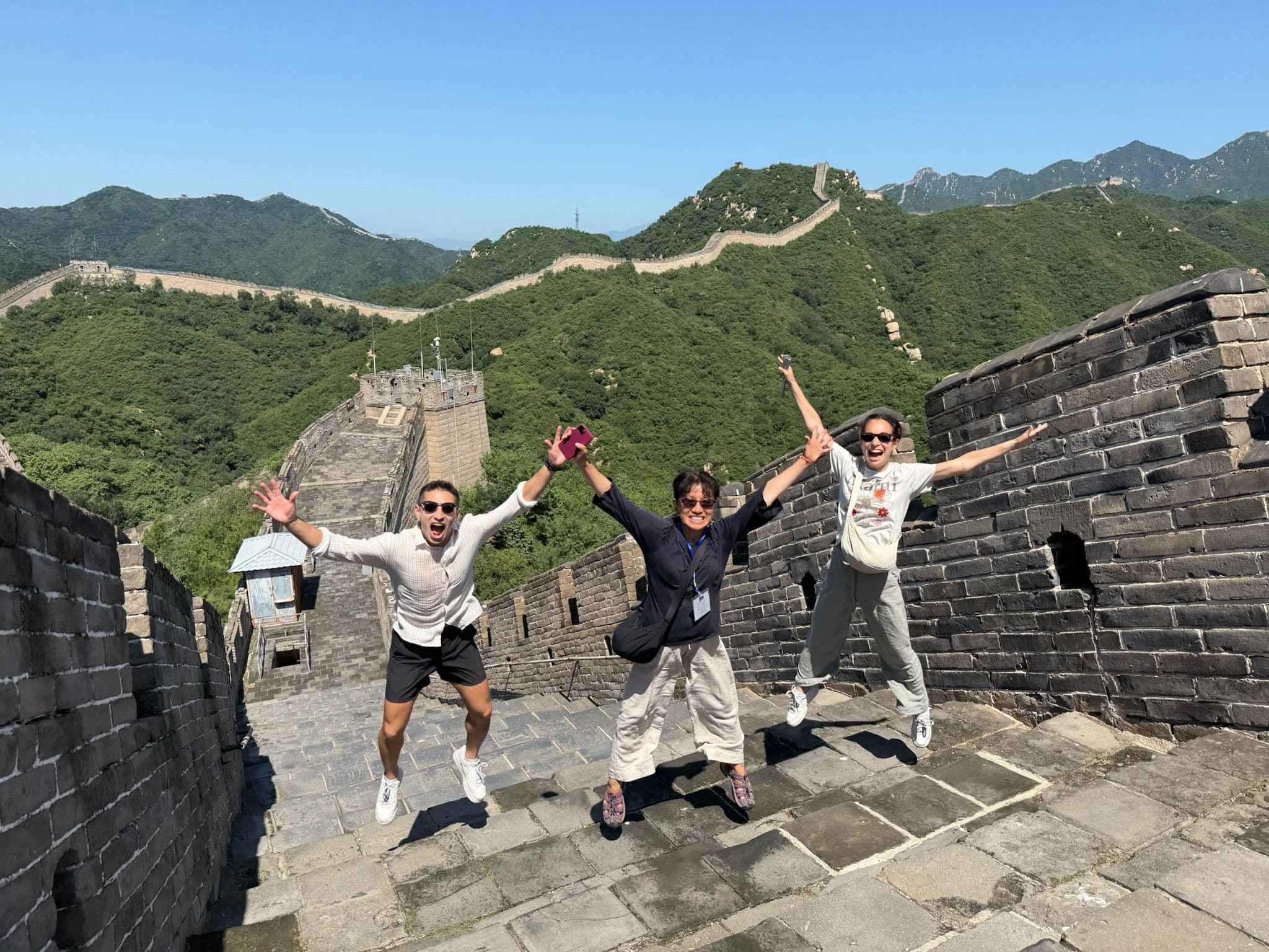 Great Wall of China with three travelers jumping and posing on a sunny, quieter section of the wall, China.