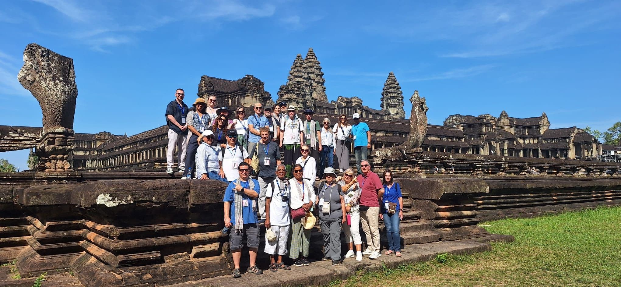 Angkor Wat temple with a large tour group posing on the temple's stone terrace in Siem Reap, Cambodia.