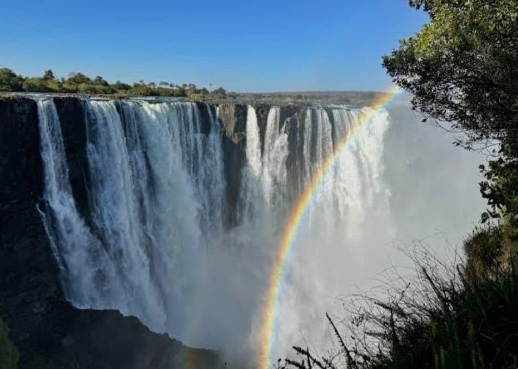 Victoria Falls waterfall with a rainbow arching through the mist, view from the Zimbabwe side.