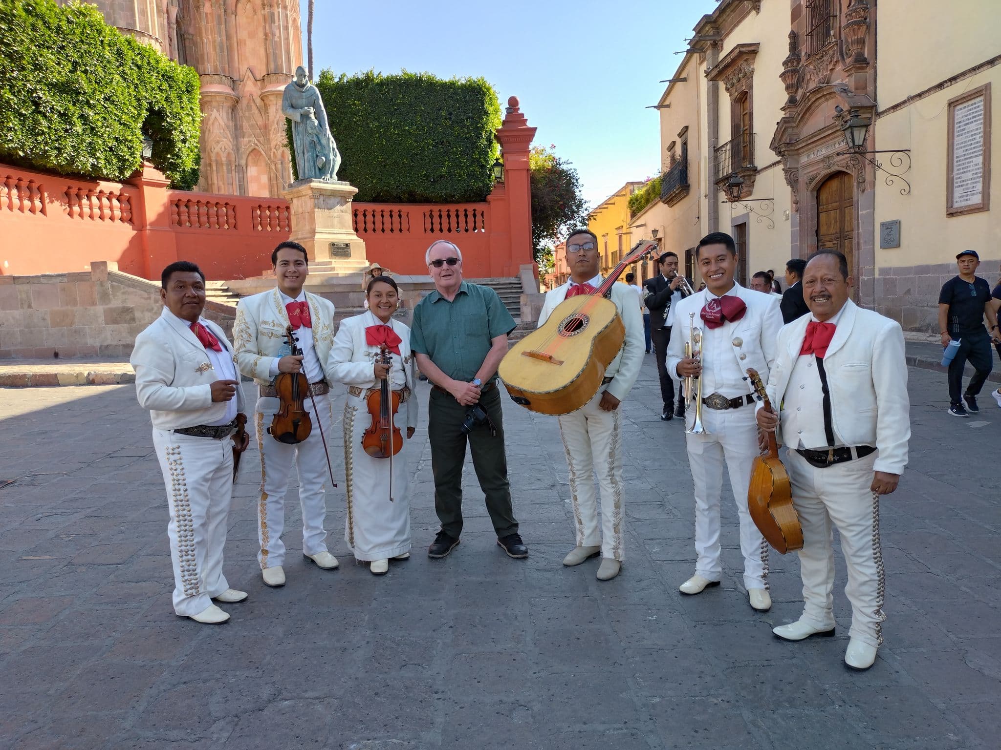 Parroquia de San Miguel Arcángel behind a mariachi band and a tourist posing for a group photo in San Miguel de Allende, Mexico.
