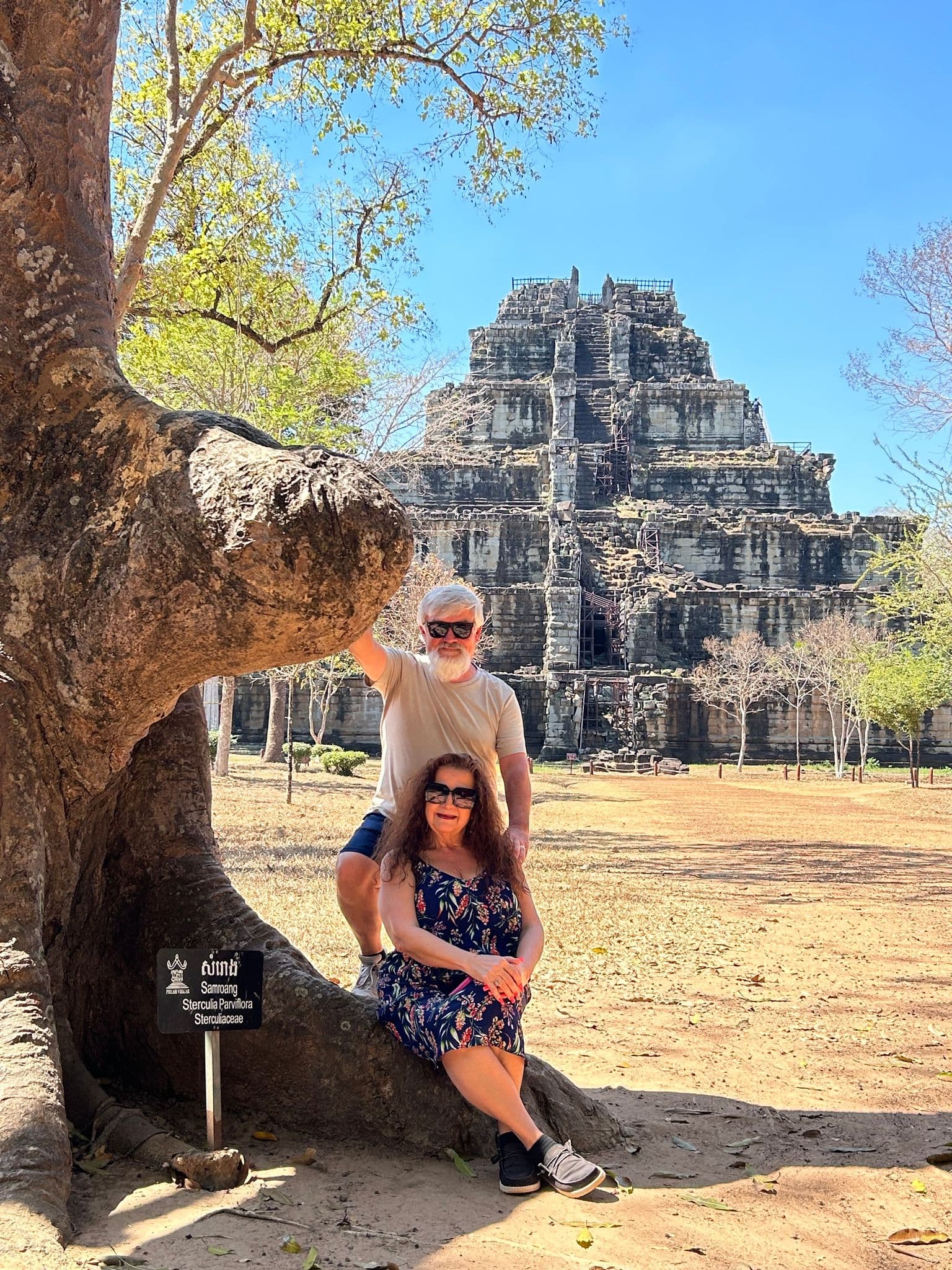 Prasat Thom pyramid temple at Koh Ker, Cambodia, rising behind a seated couple by a large tree.