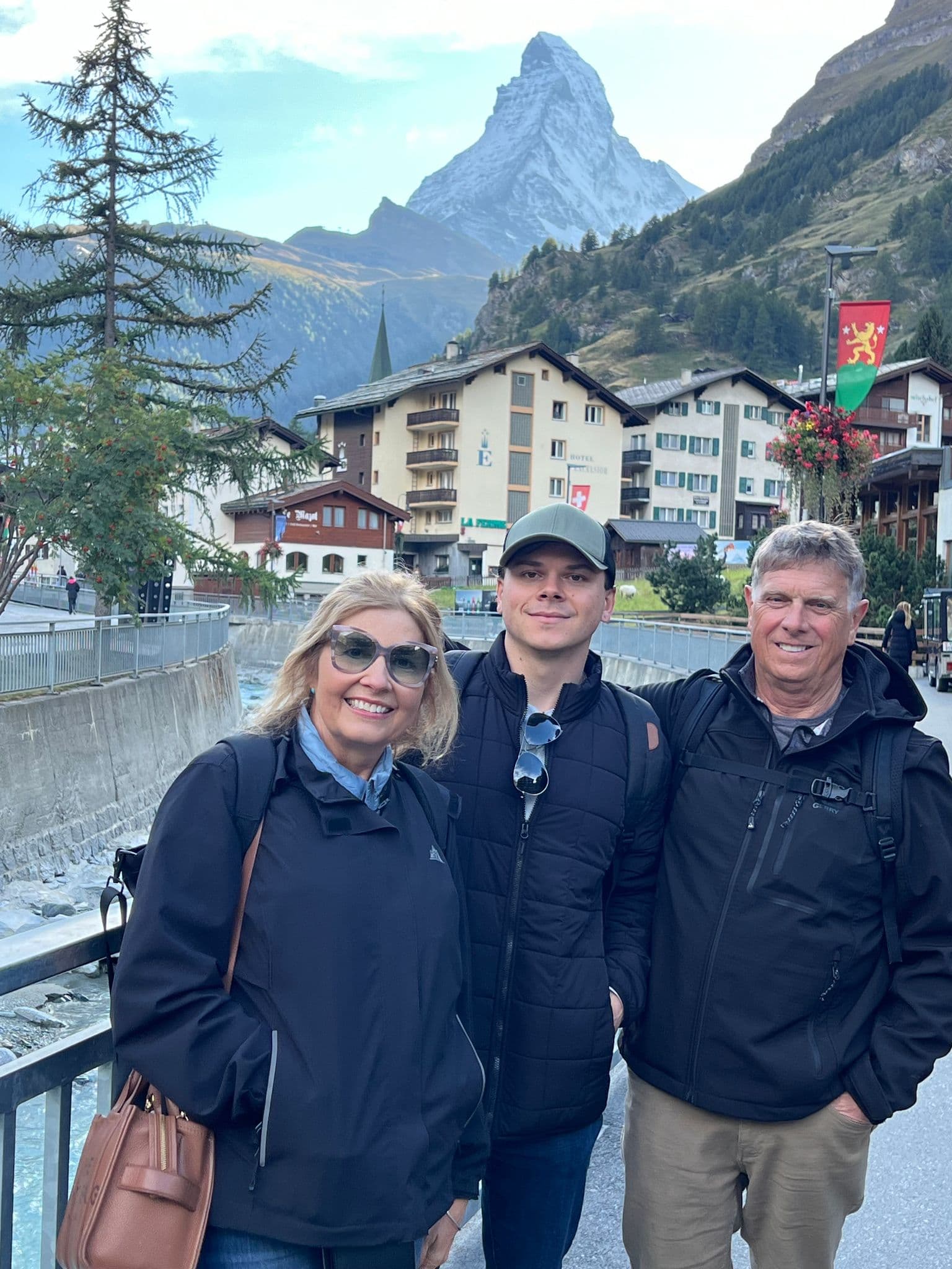Matterhorn towering above three travelers posing on a bridge in Zermatt, Switzerland.