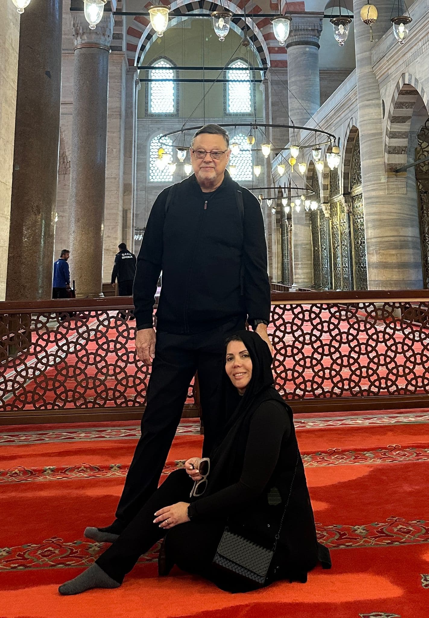 Interior of Hagia Sophia (Ayasofya) in Istanbul, Turkey with two travelers posing on a red prayer carpet.