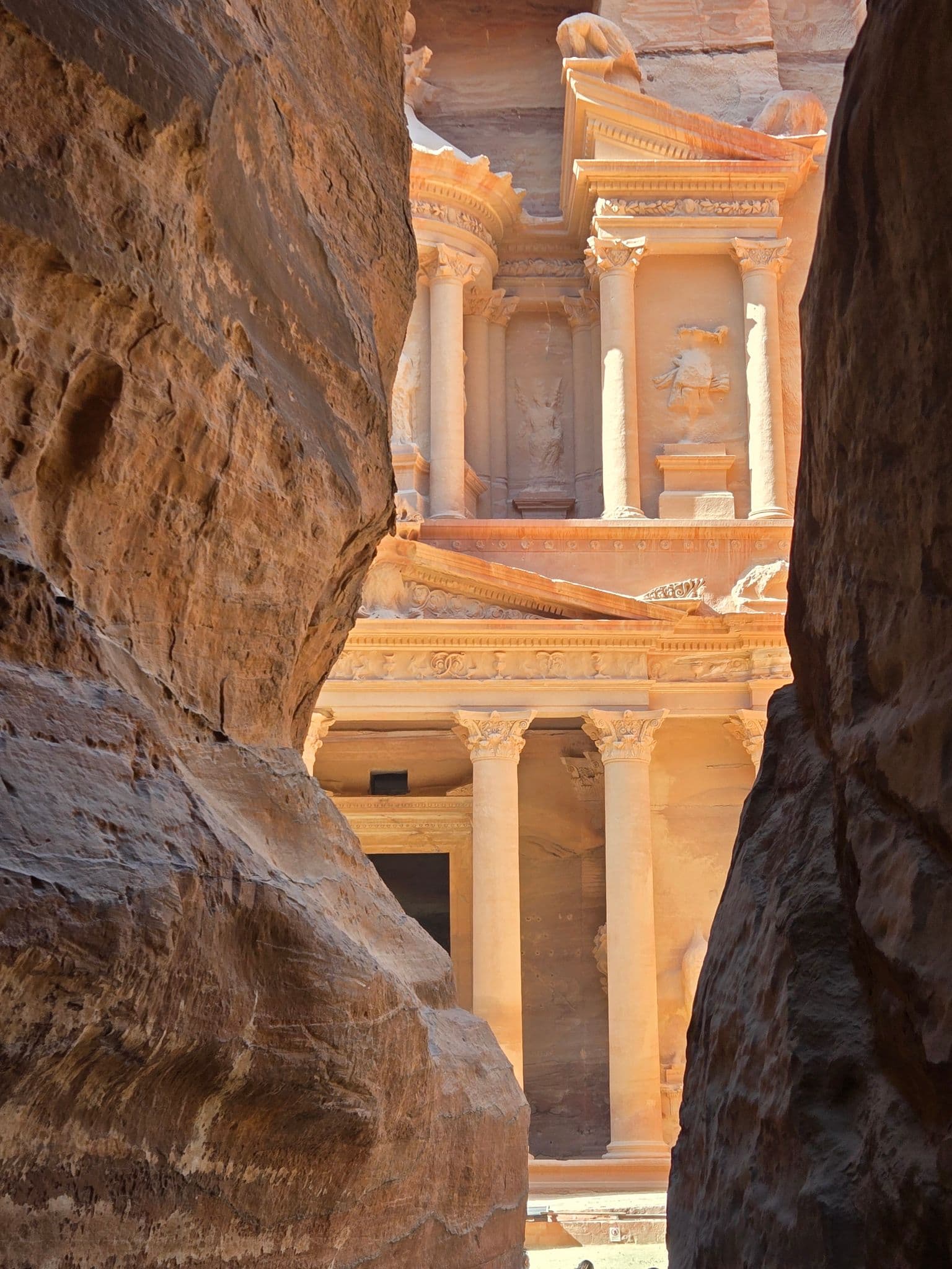 Al-Khazneh (the Treasury) framed by the Siq's sandstone walls, sunlight on the carved façade in Petra, Jordan.