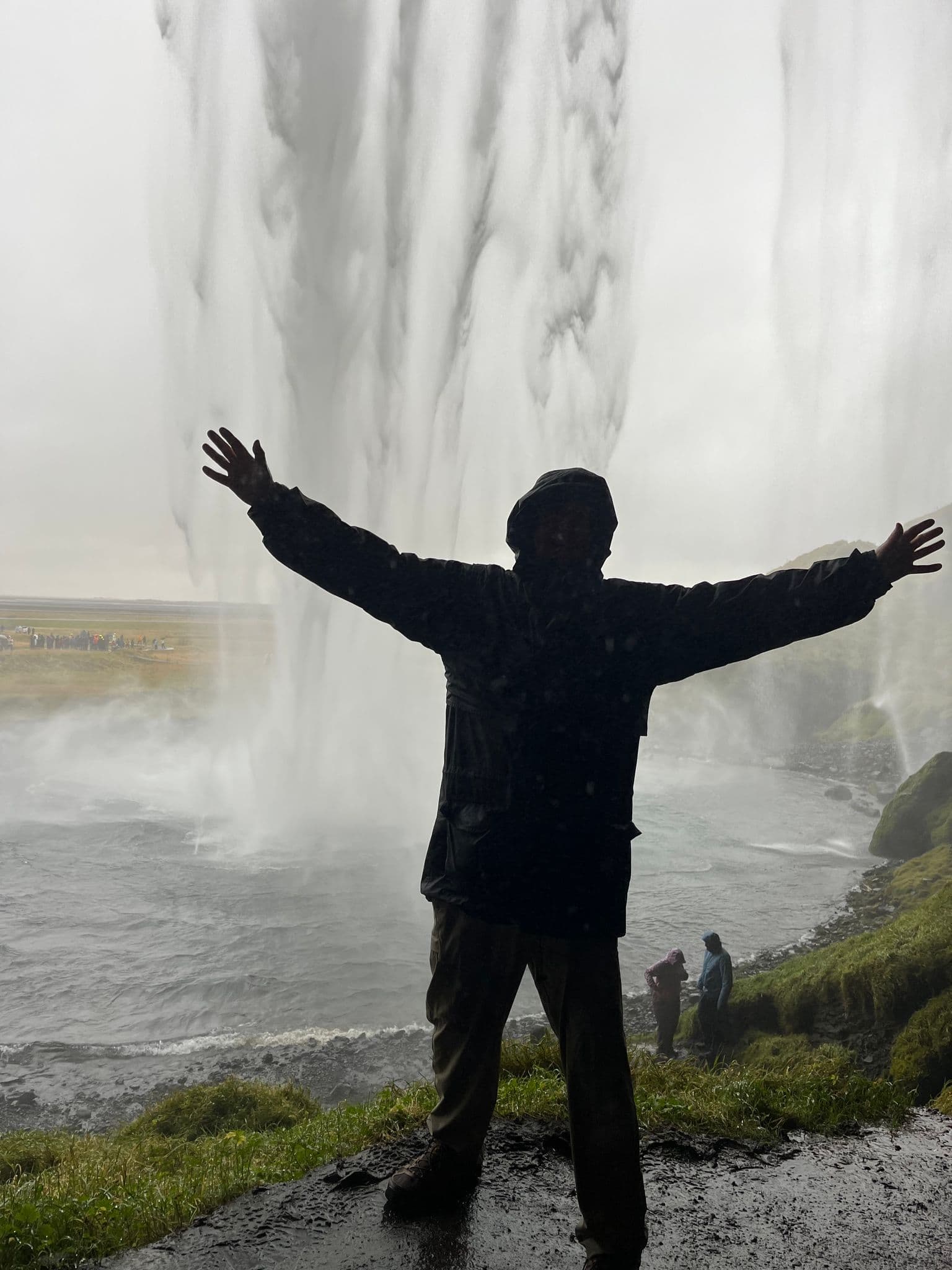 Seljalandsfoss waterfall with a silhouetted person standing with arms outstretched behind the falls, Iceland.
