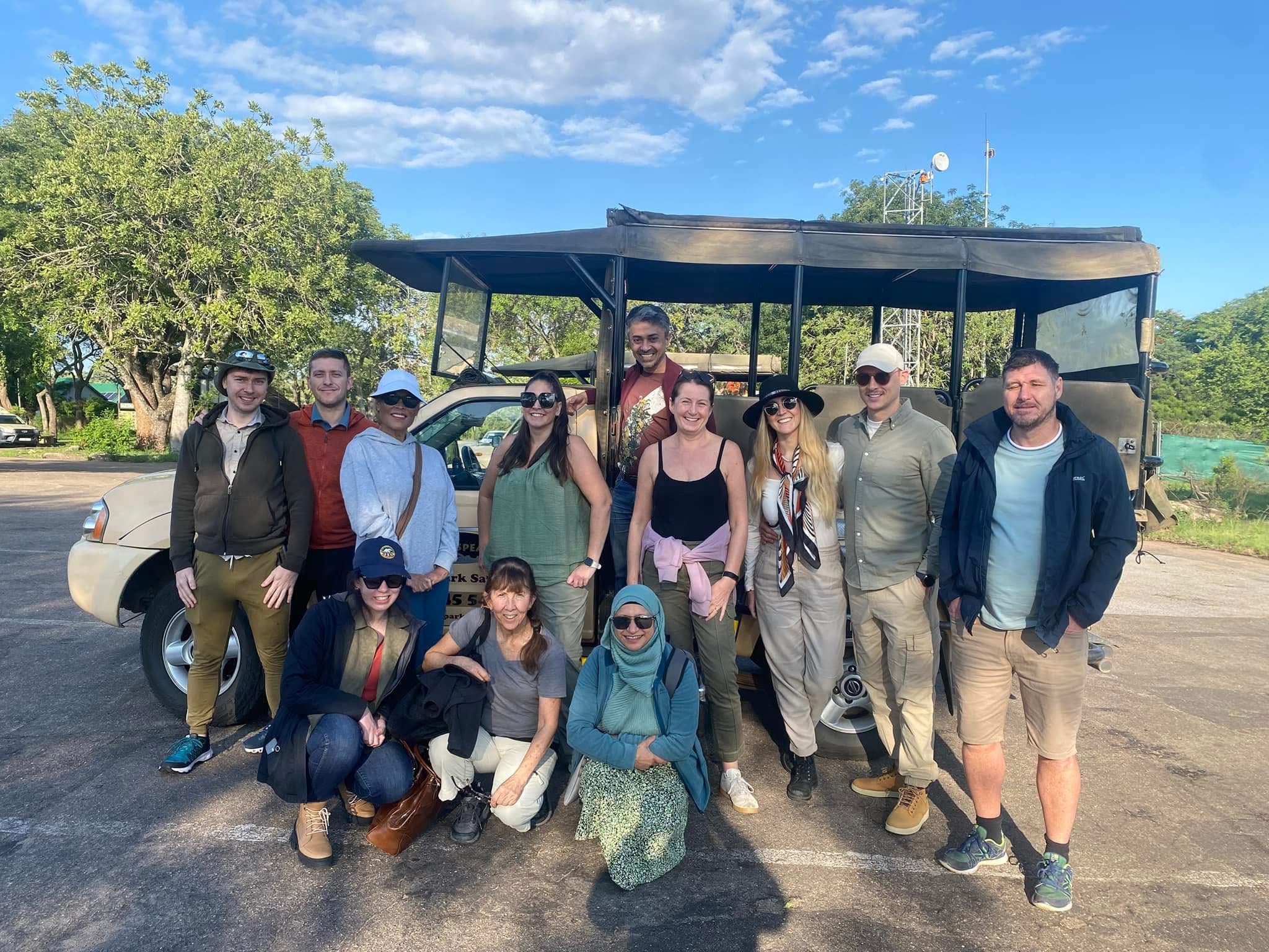 Group of travelers posing by an open safari vehicle at Kruger National Park, South Africa, before a game drive.