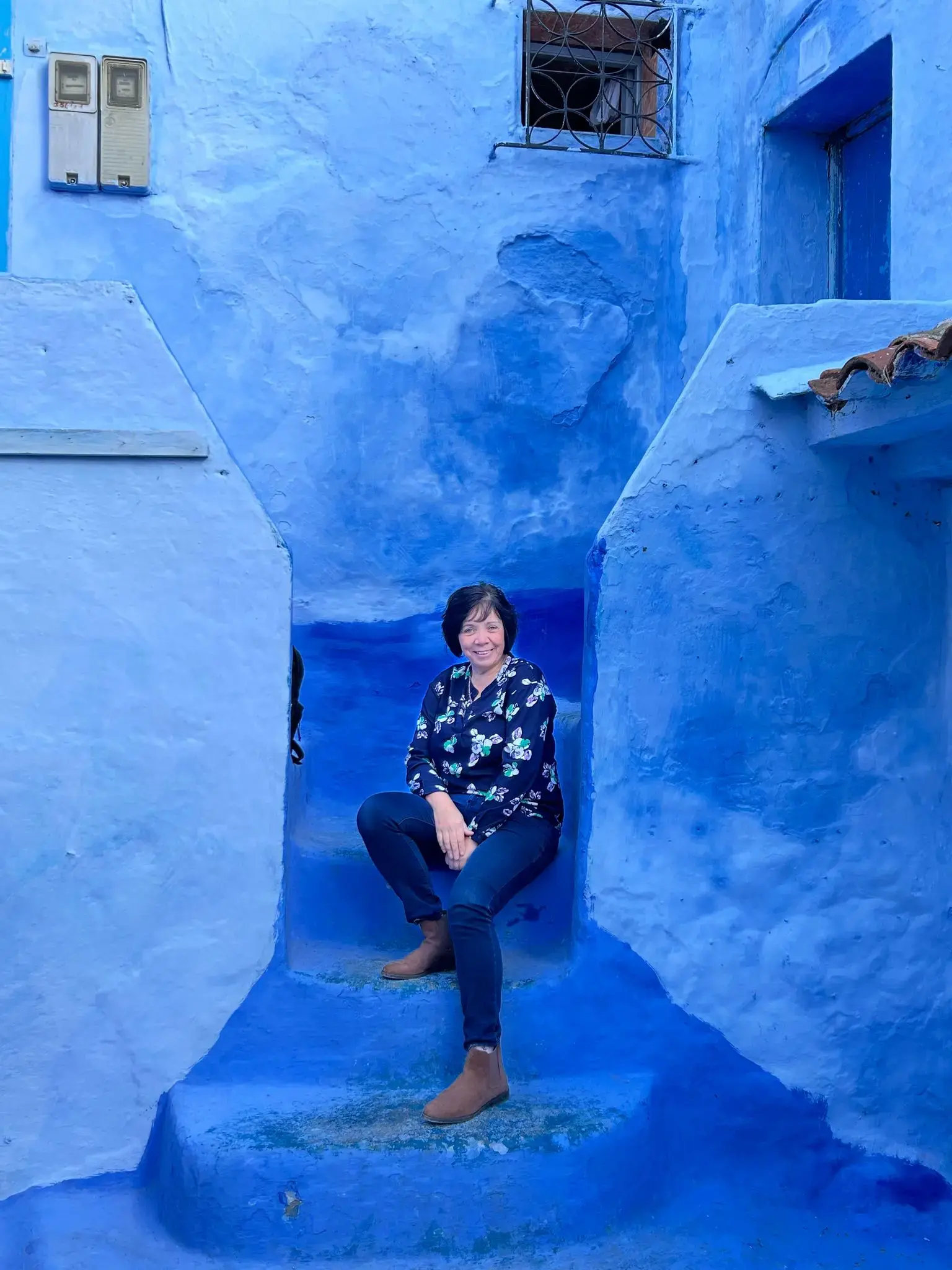 Blue-painted walls and steps in the Chefchaouen medina, Morocco, with a woman sitting on the stairs.