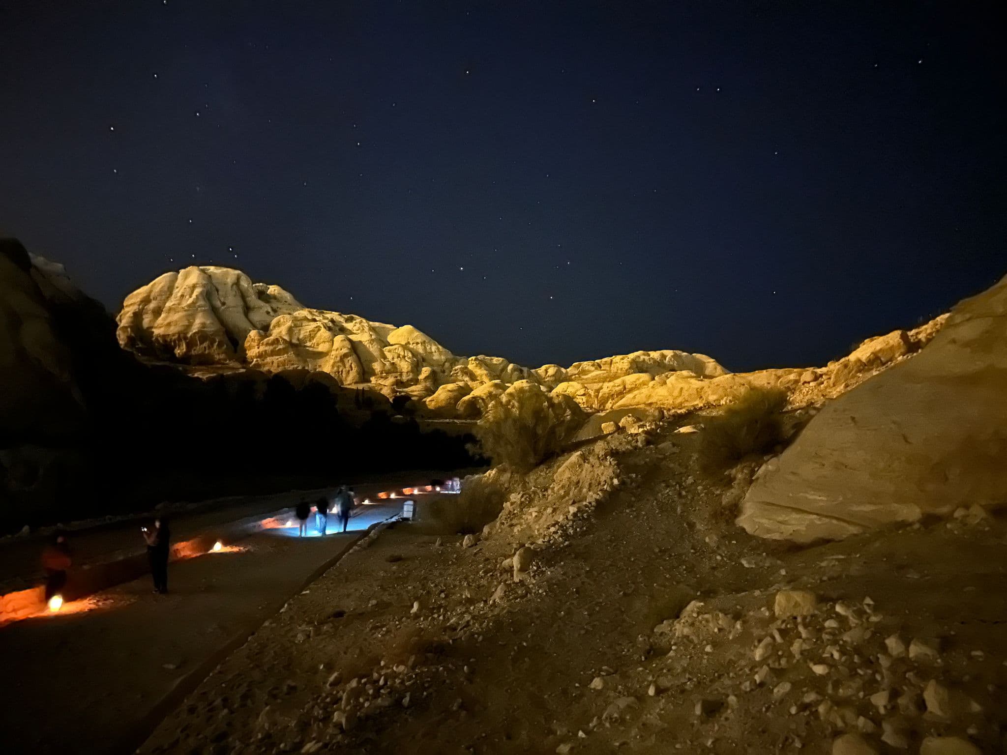 Illuminated sandstone cliffs and a lantern-lit path into Petra with people walking at night, Petra, Wadi Musa, Jordan.