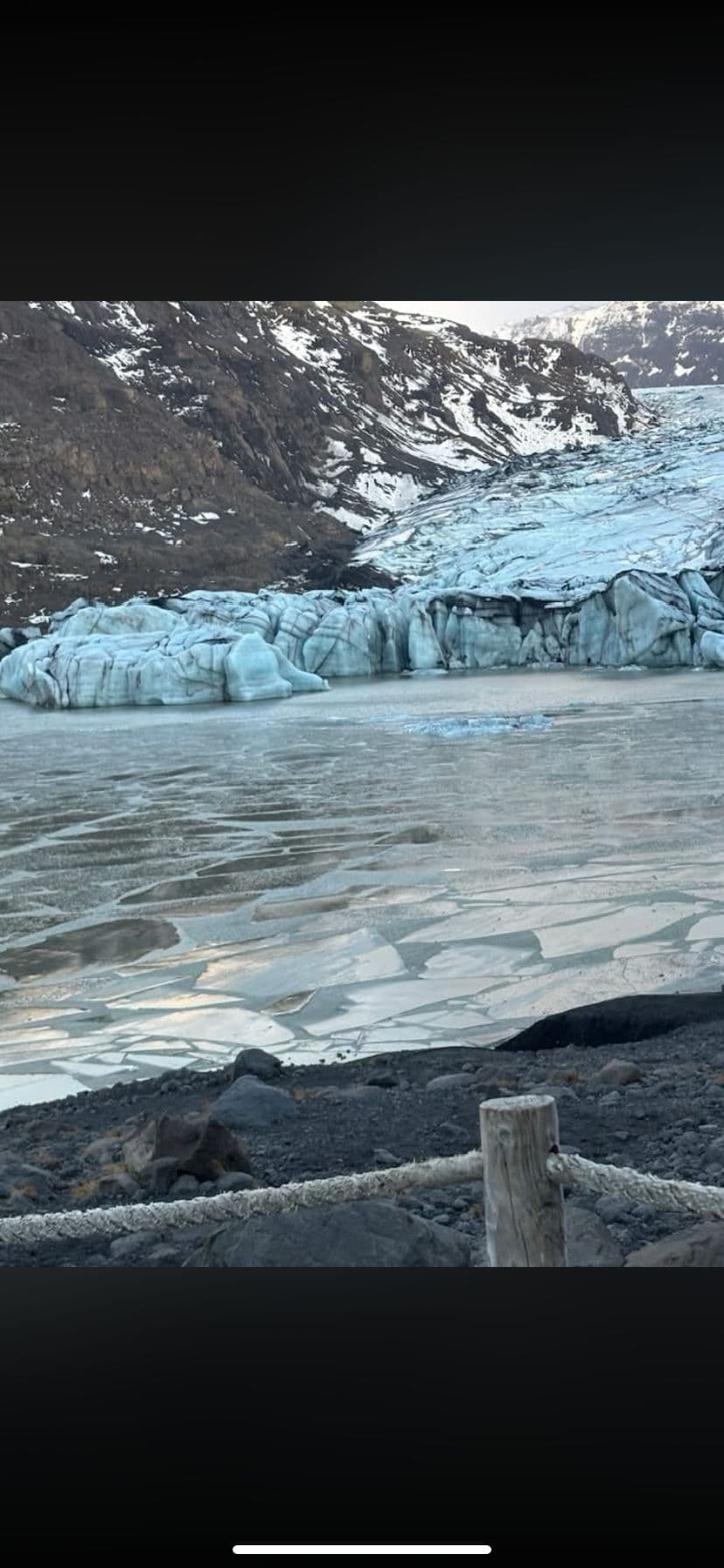 Blue glacier front and partly frozen glacial lake with rocky shoreline and a rope fence, Iceland.