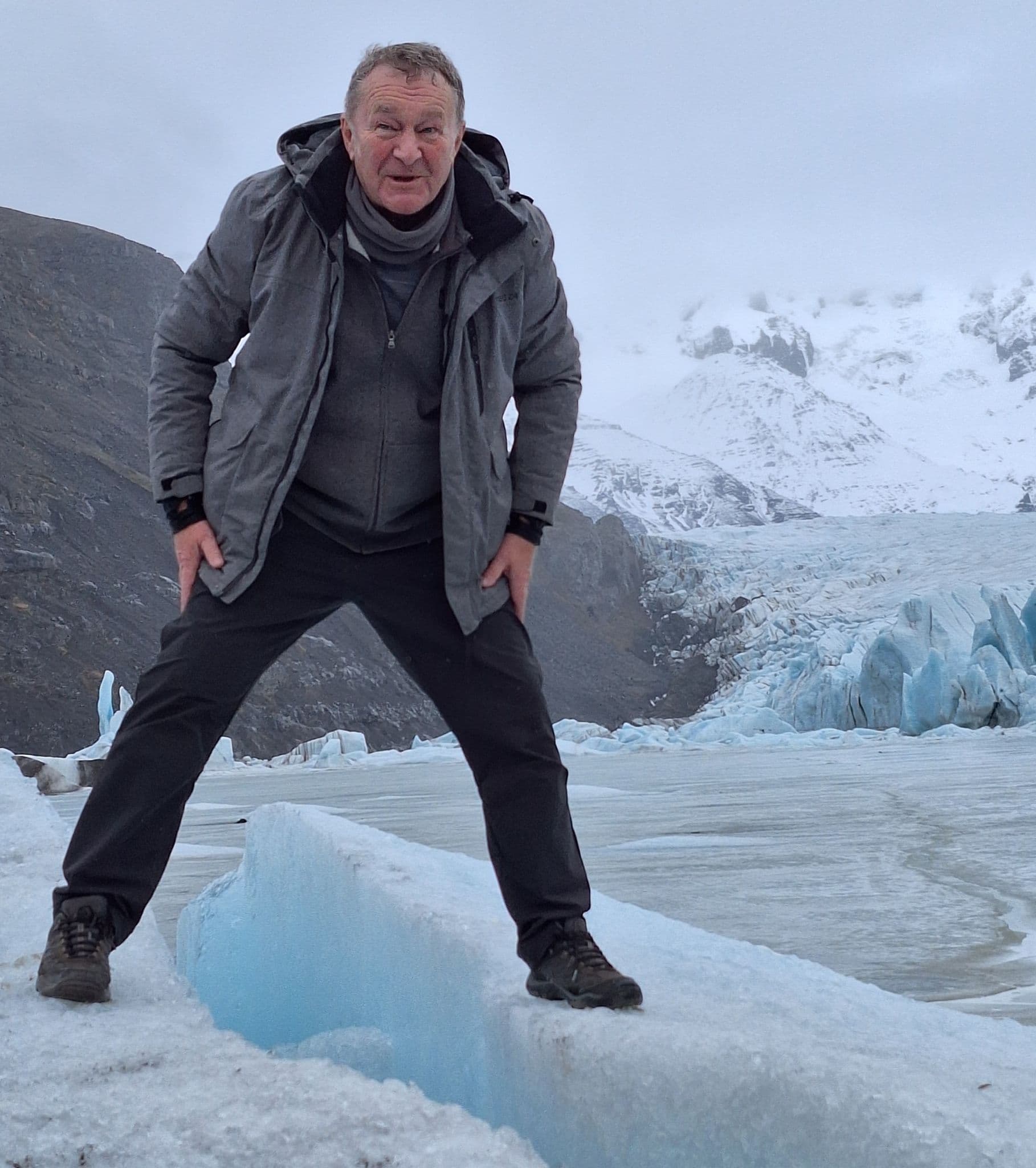 Man standing on blue glacier ice with snowy mountains and a glacier tongue behind at Svínafellsjökull, Iceland.