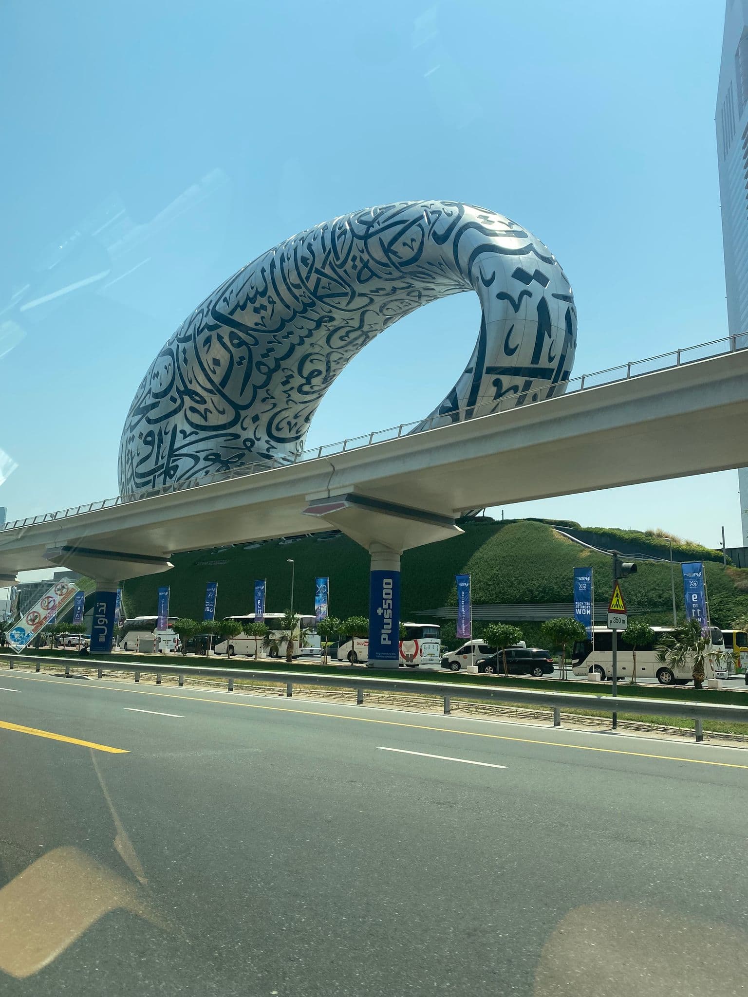 Museum of the Future, a torus-shaped building covered in Arabic calligraphy, rising above a highway with tour buses in Dubai, United Arab Emirates.