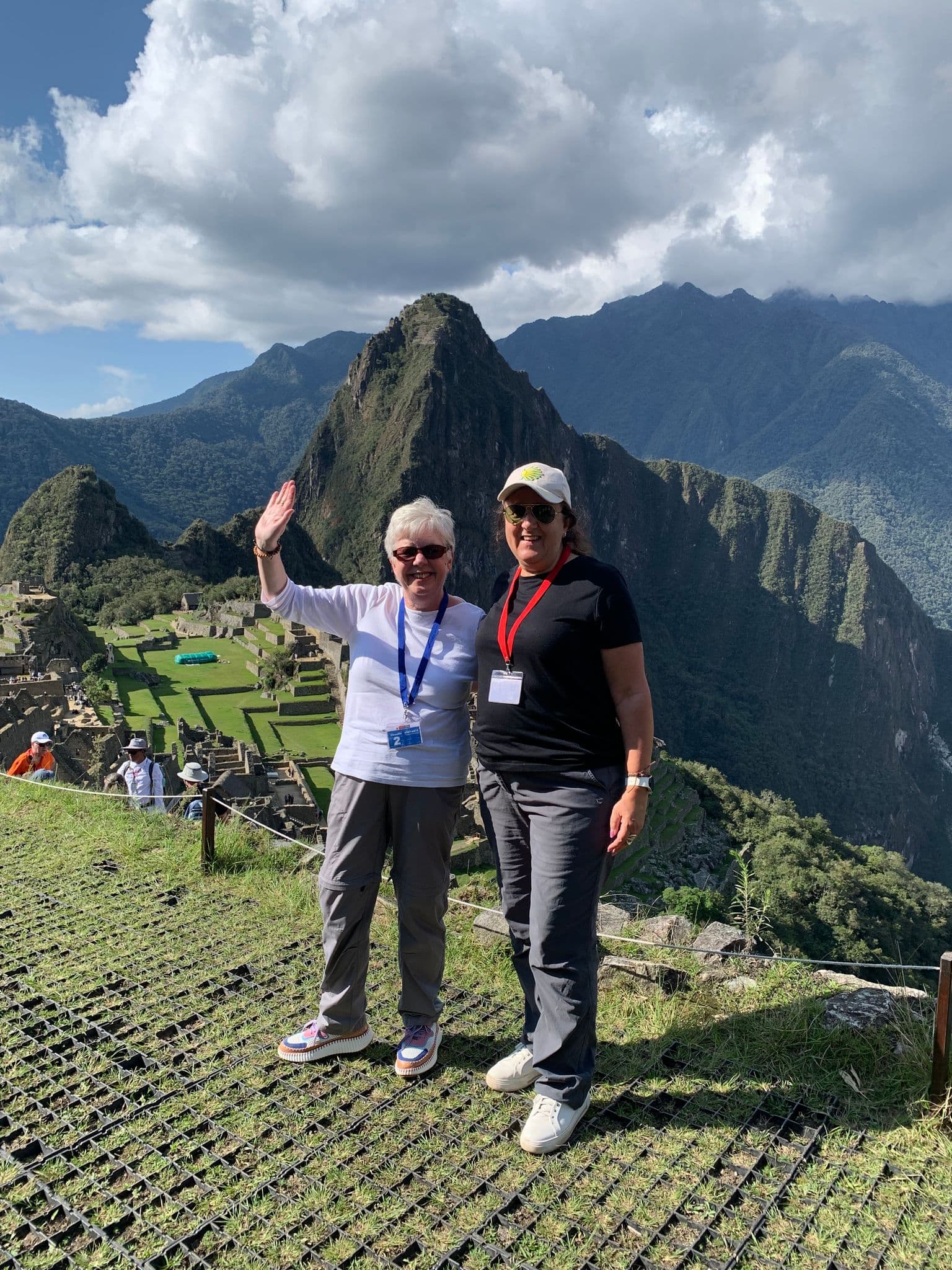 Machu Picchu ruins with Huayna Picchu peak in the background and two travelers posing at an overlook, Peru.