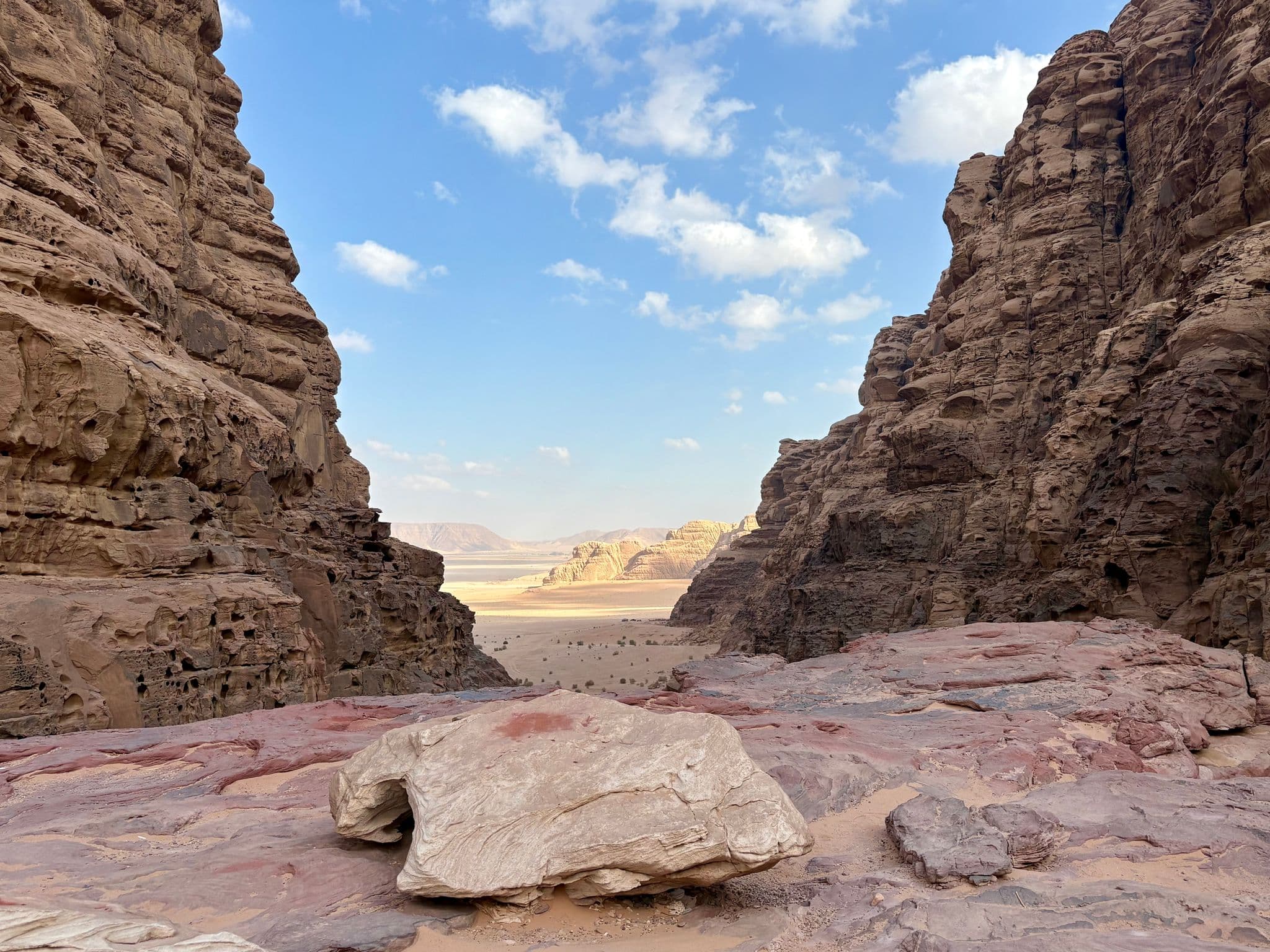 Red sandstone cliffs framing a wide desert valley in Wadi Rum, Jordan, with layered rocks in the foreground under a blue sky