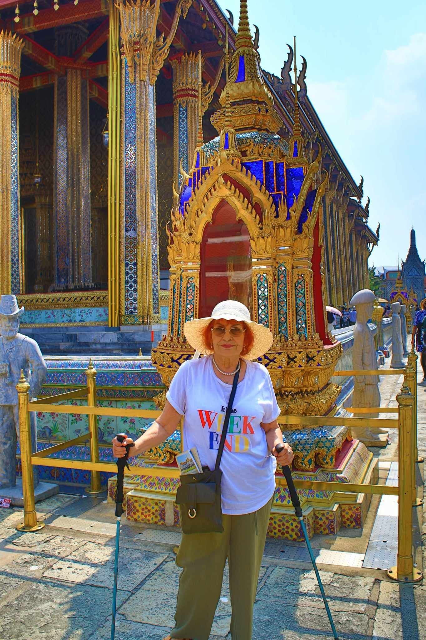 Gilded shrine at Wat Phra Kaew, Grand Palace, Bangkok, Thailand, with a tourist woman posing with walking poles.