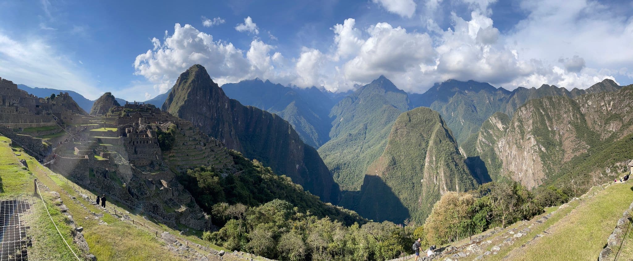 Machu Picchu ruins on stone terraces with hikers and Huayna Picchu rising behind, Andes near Cusco, Peru.