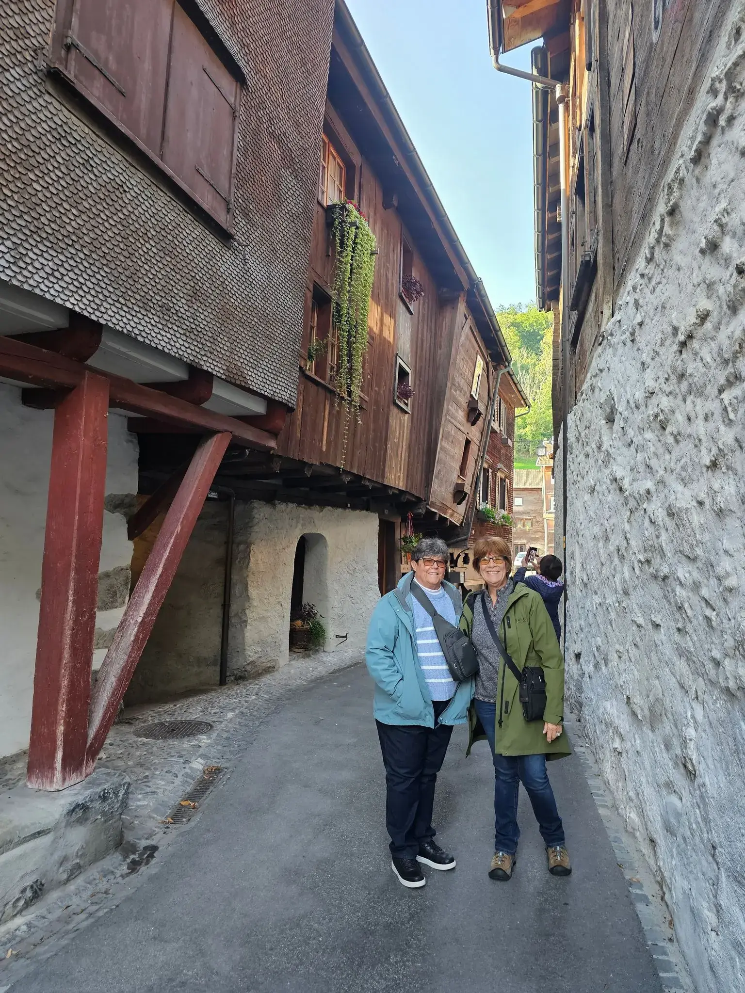 Narrow historic street in Old Zermatt with two travelers posing between overhanging wooden houses, Zermatt, Switzerland.