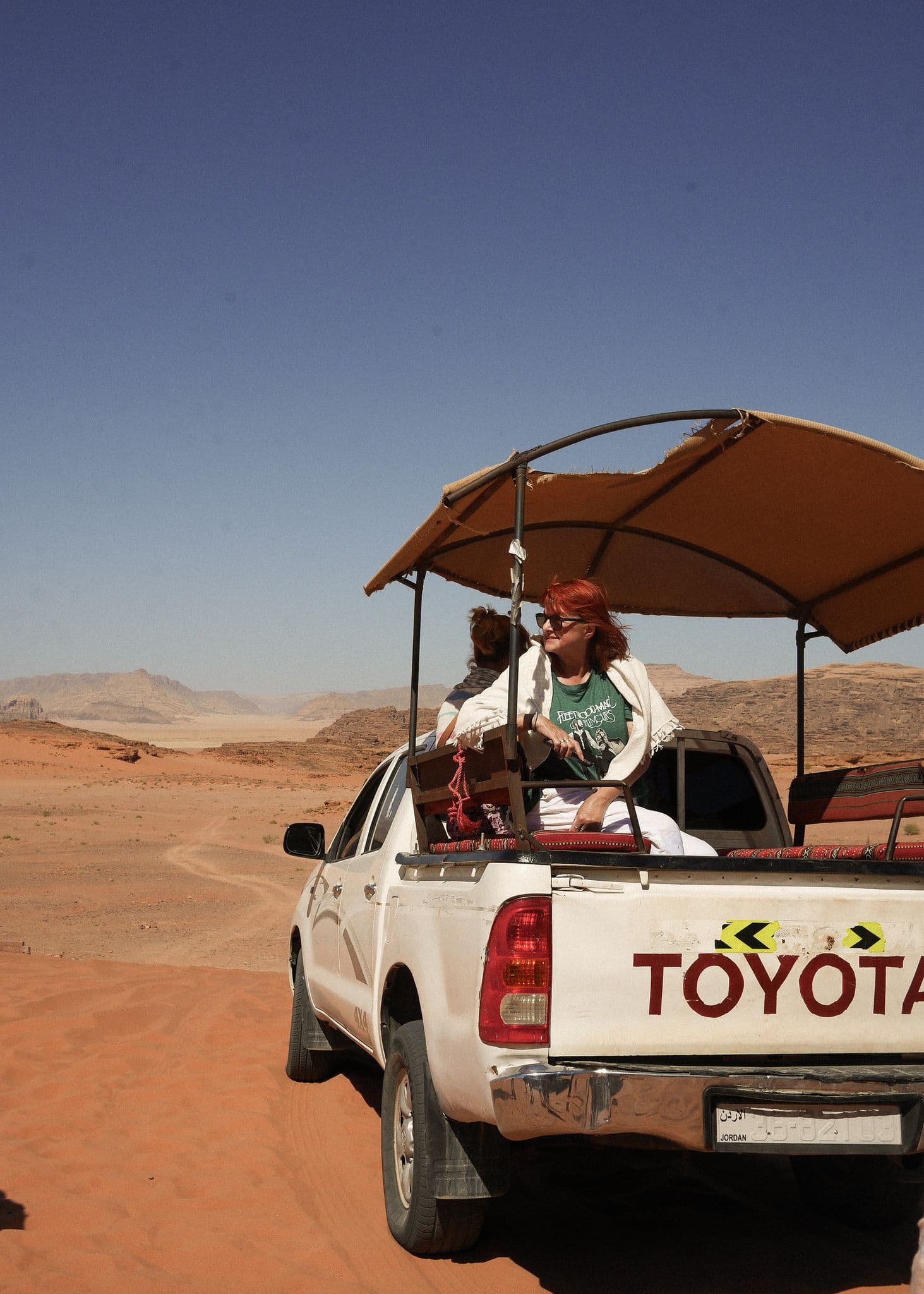 Wadi Rum desert landscape with a covered pickup truck carrying travelers on a sandy tour, Jordan.
