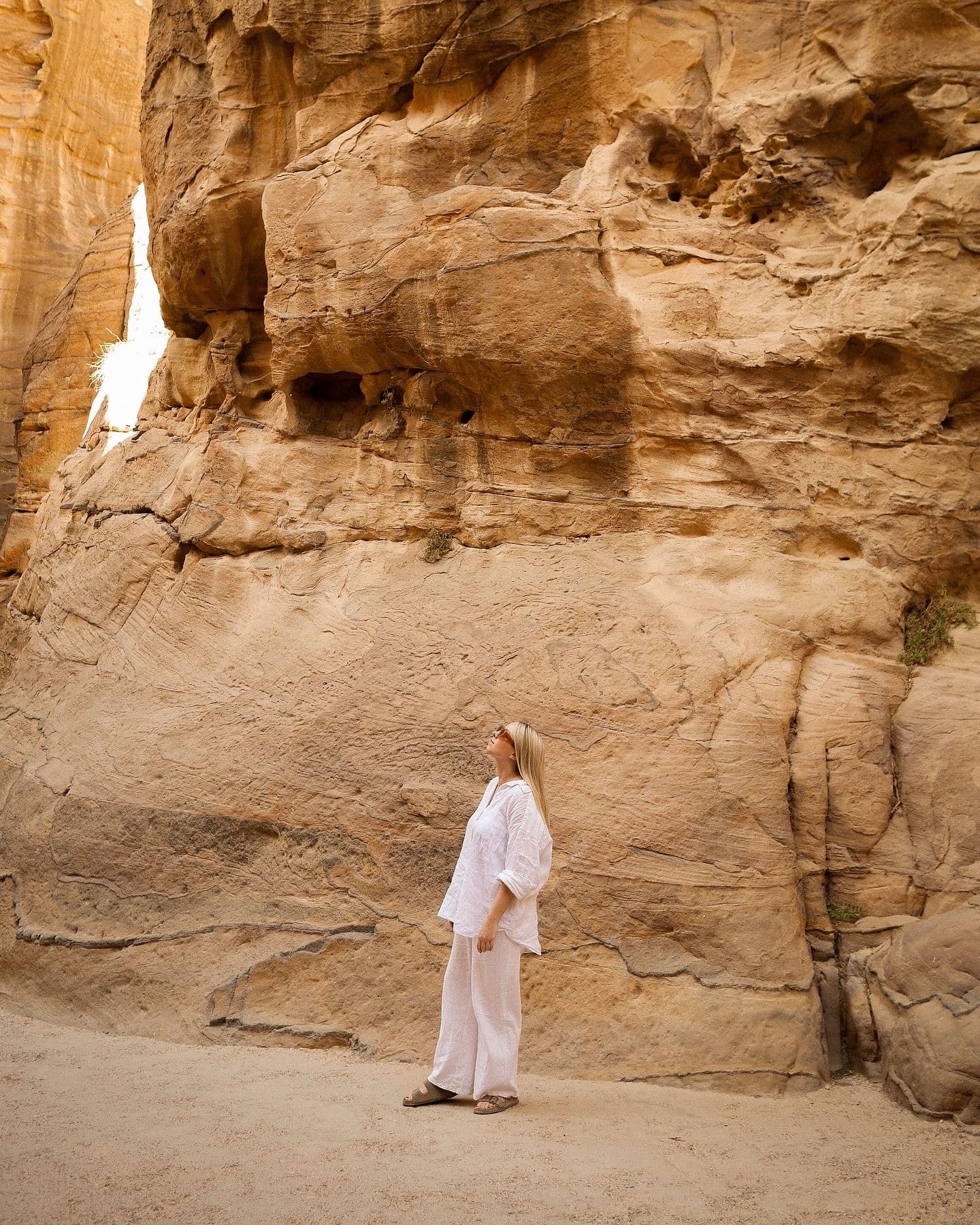Sandstone canyon wall at the Siq, Petra, Jordan, with a woman in white standing and looking up on a trip.