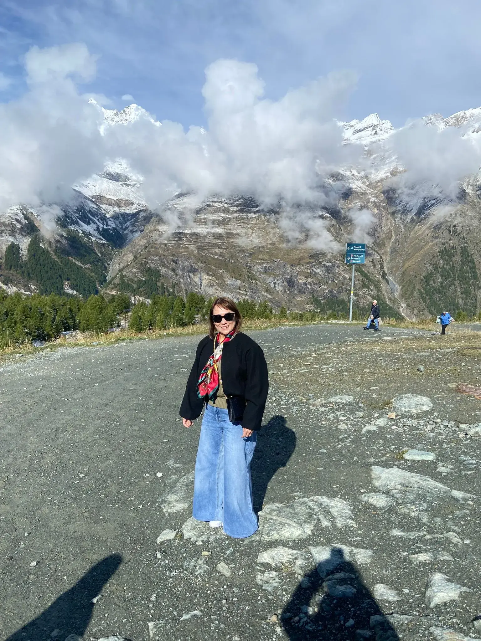 Snow-capped Matterhorn and alpine slopes with a person standing on a gravel viewpoint in Zermatt, Switzerland.