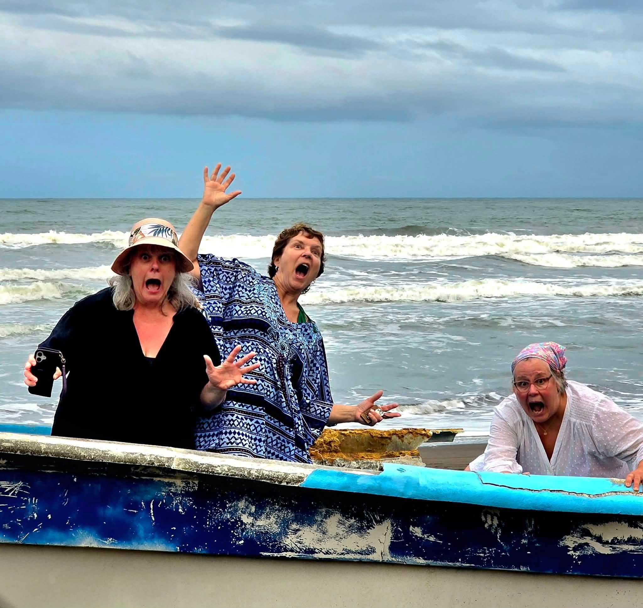 Three women leaning on a small boat, making surprised faces on a beach in Tortuguero, Costa Rica.