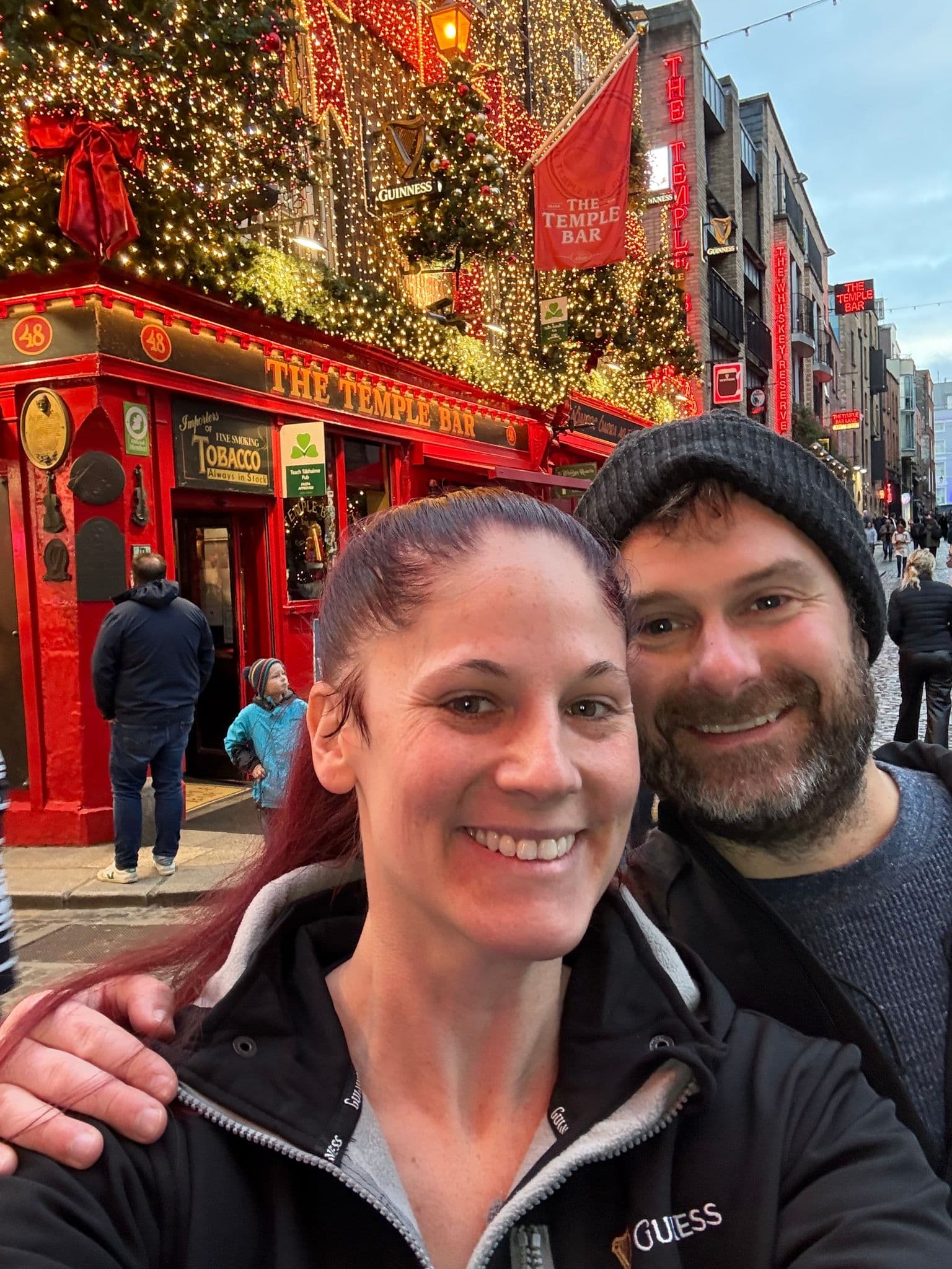 The Temple Bar pub in Dublin, Ireland, with two travelers taking a selfie outside its decorated, light-covered facade.