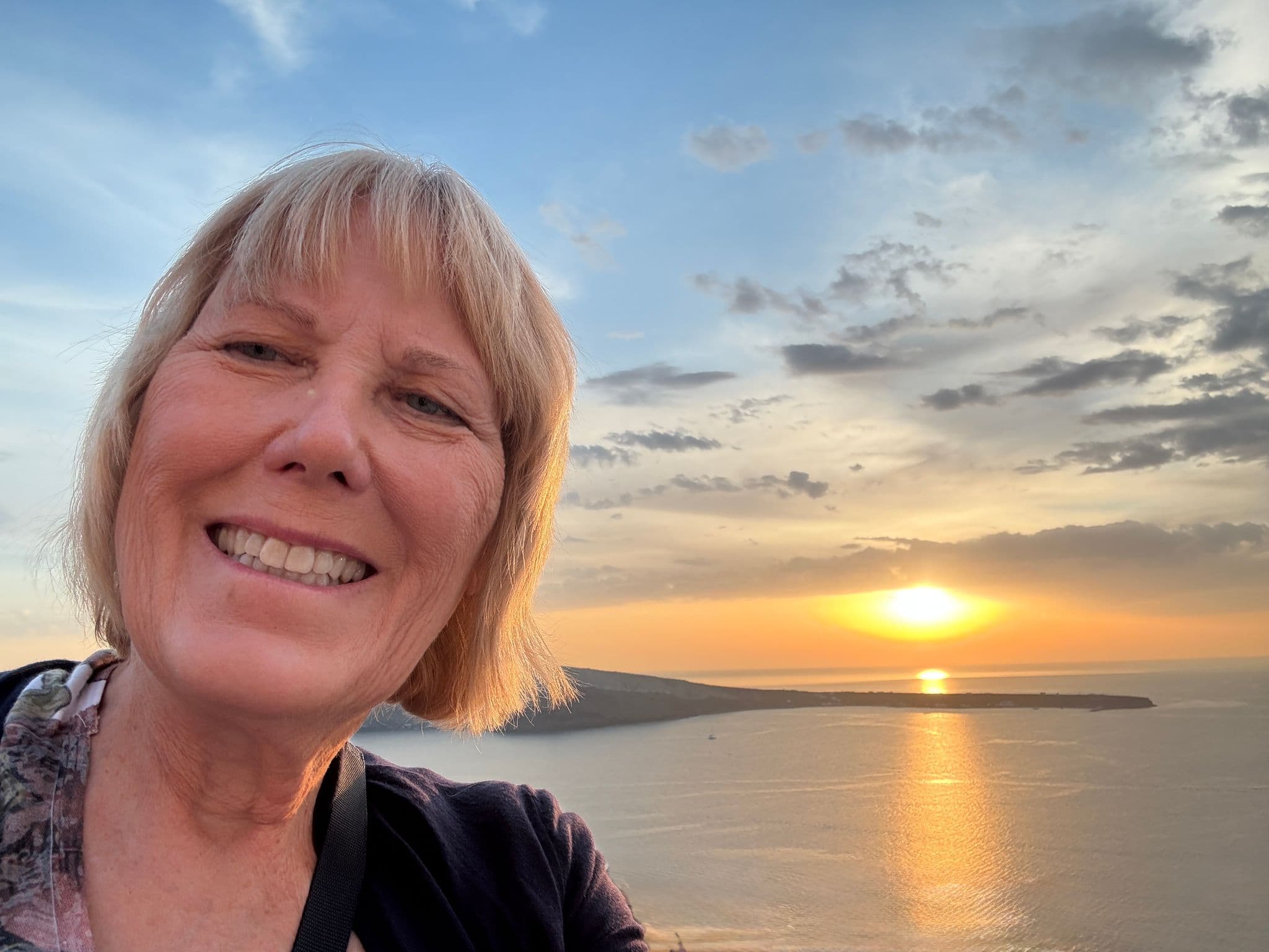 Sunset over Oia, Santorini, Greece with a smiling traveler taking a selfie as the sun reflects on the caldera