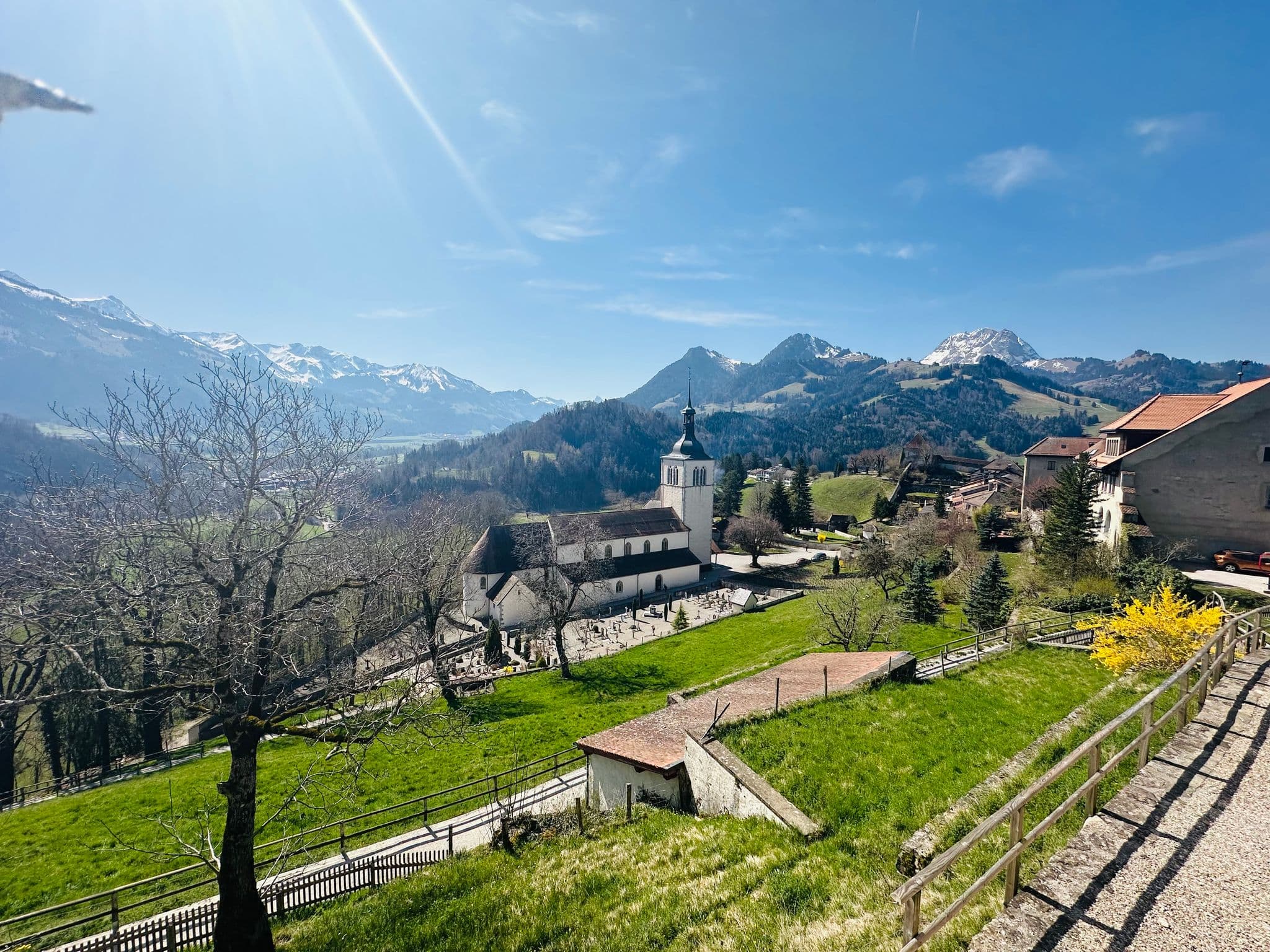 Hilltop church and village of Gruyères with green pastures and snow-capped Alps in the background, Gruyères, Switzerland.