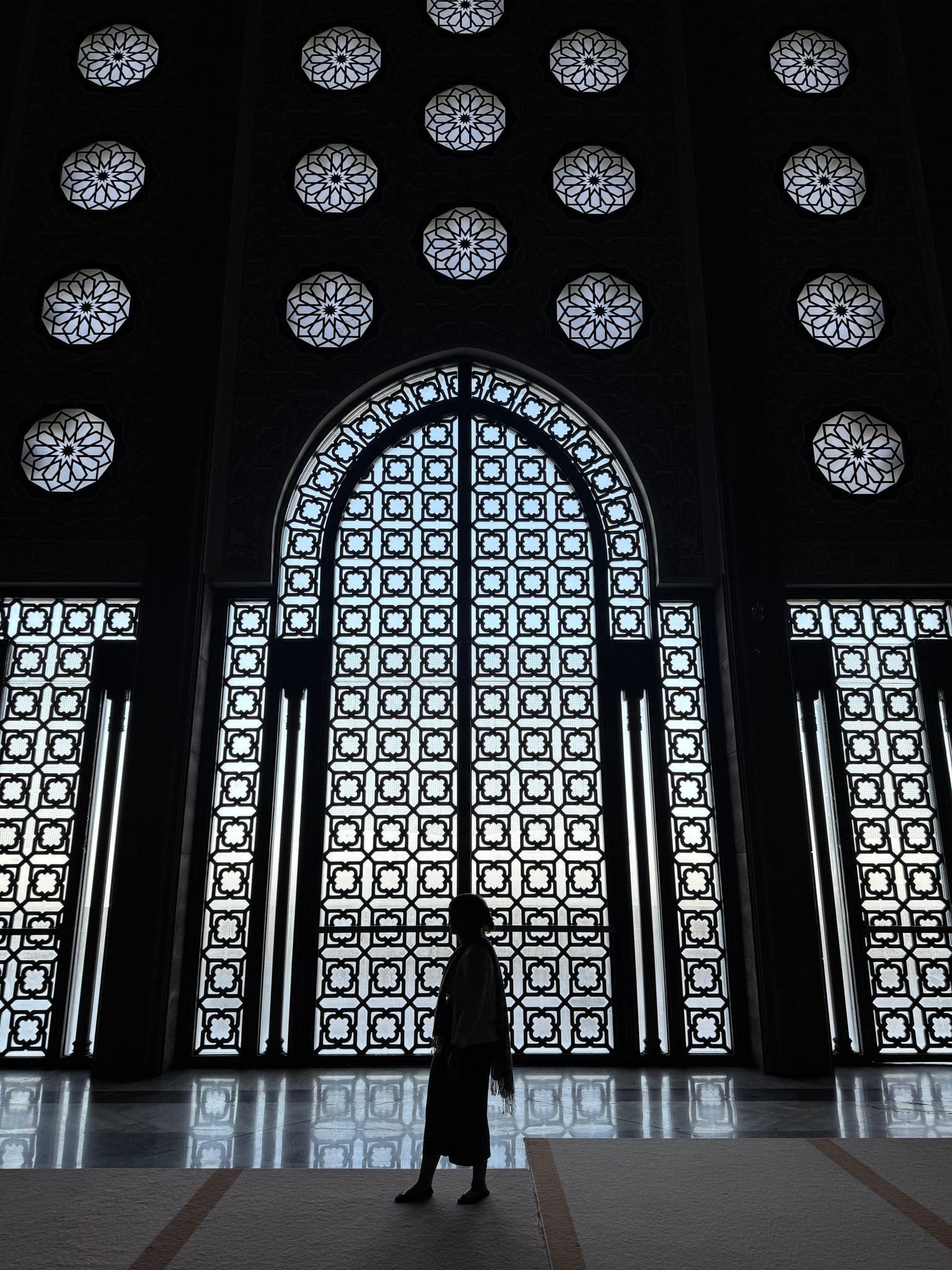 Hassan II Mosque large arched patterned window and carved screens with a silhouetted person walking inside, Casablanca, Morocco.
