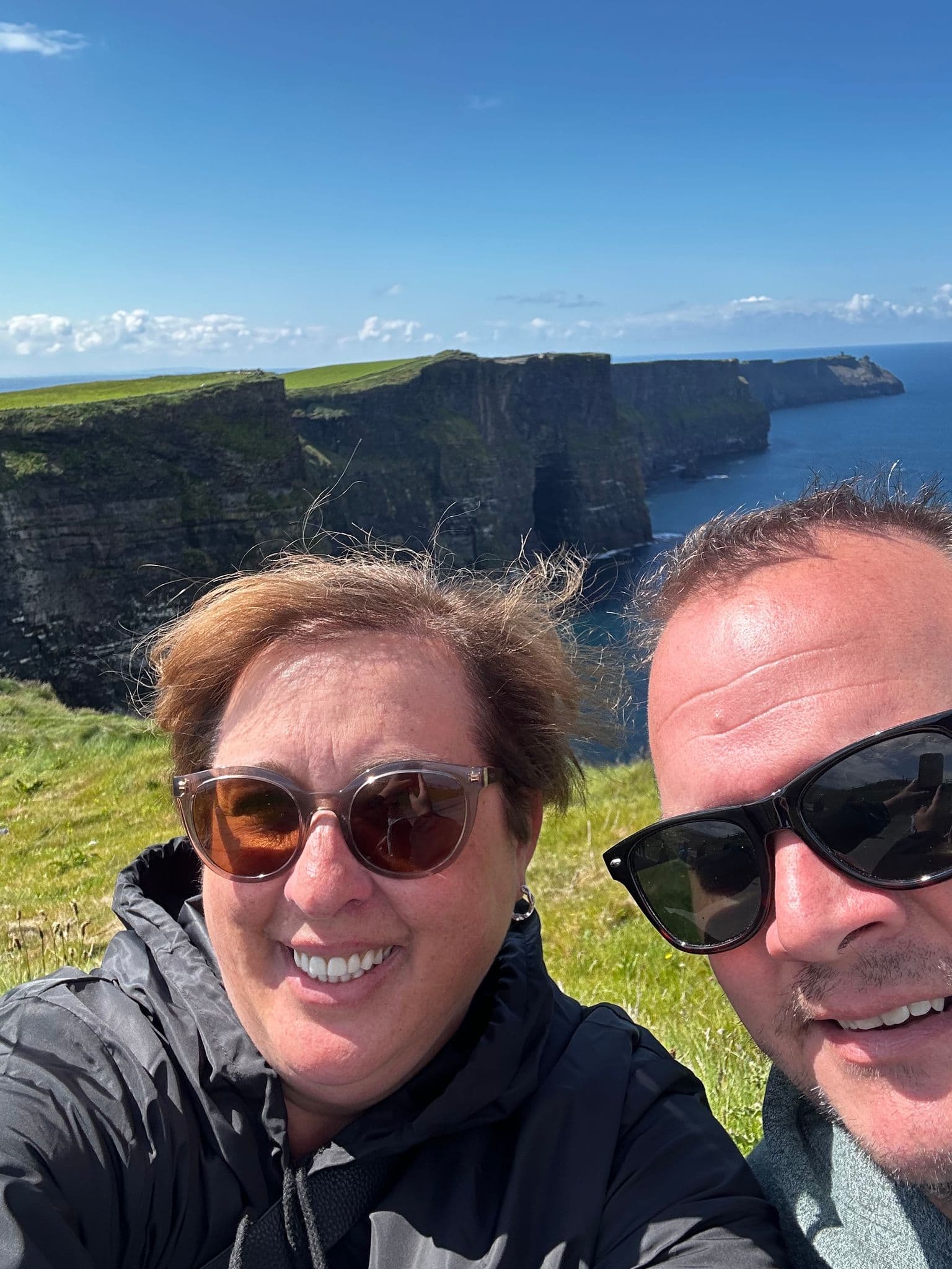 Cliffs of Moher with two travelers taking a selfie on the grassy cliff edge, County Clare, Ireland.