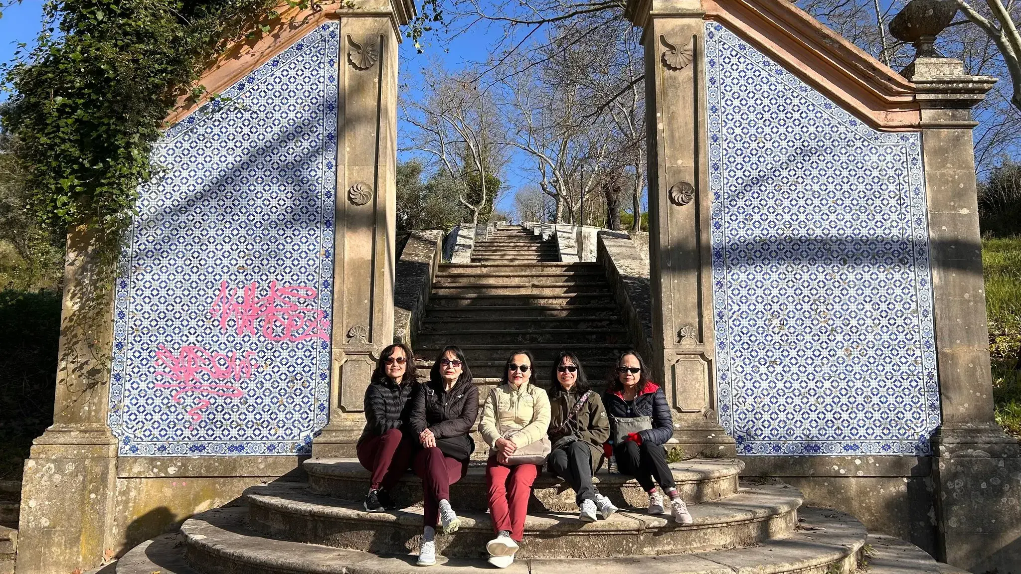 Blue-and-white tiled panels and a stone staircase with five women sitting on the lower steps, Tomar, Portugal.