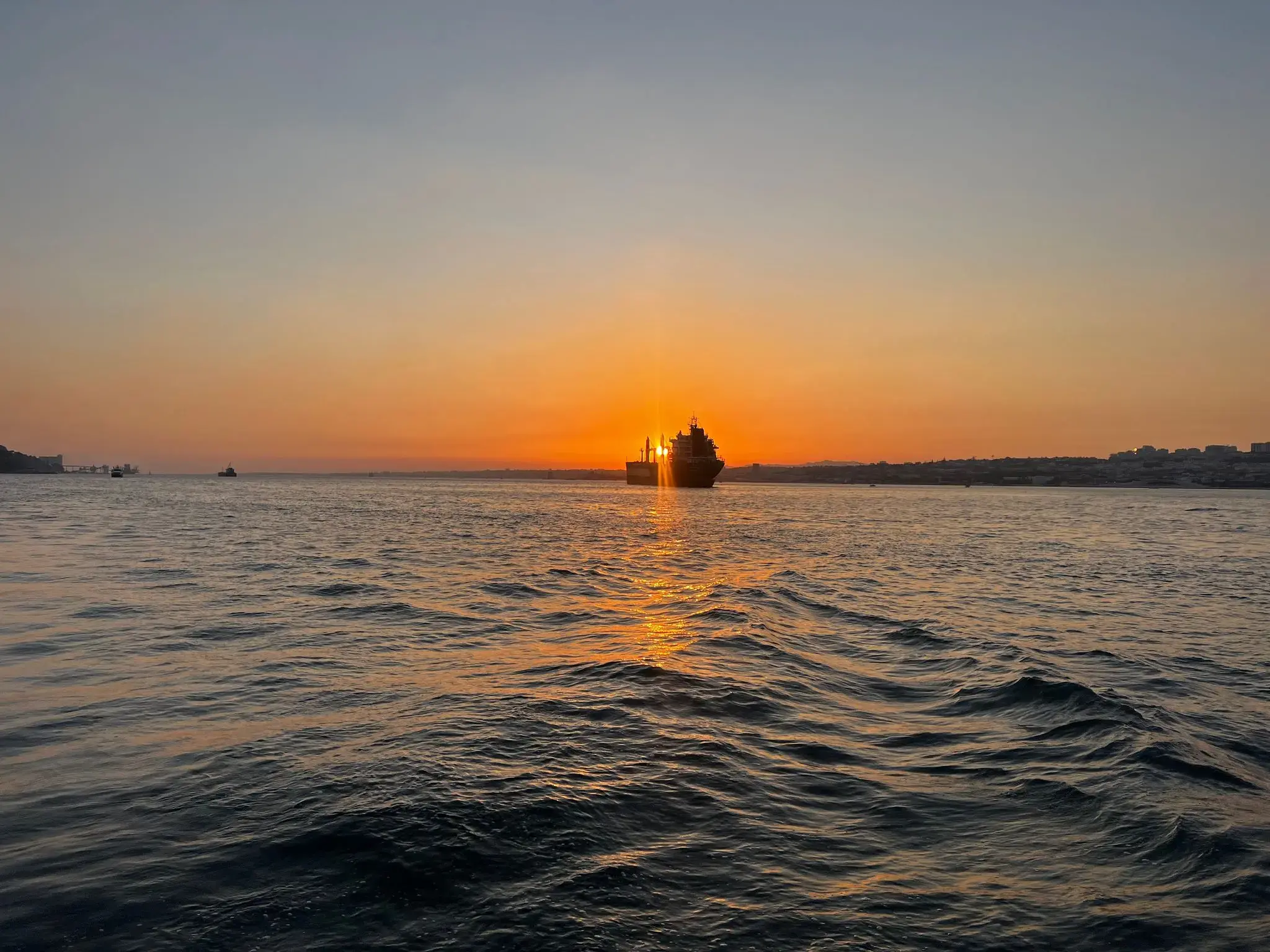 Sunset behind a silhouetted ship on the Tagus River, Lisbon, Portugal, with rippling water in the foreground.