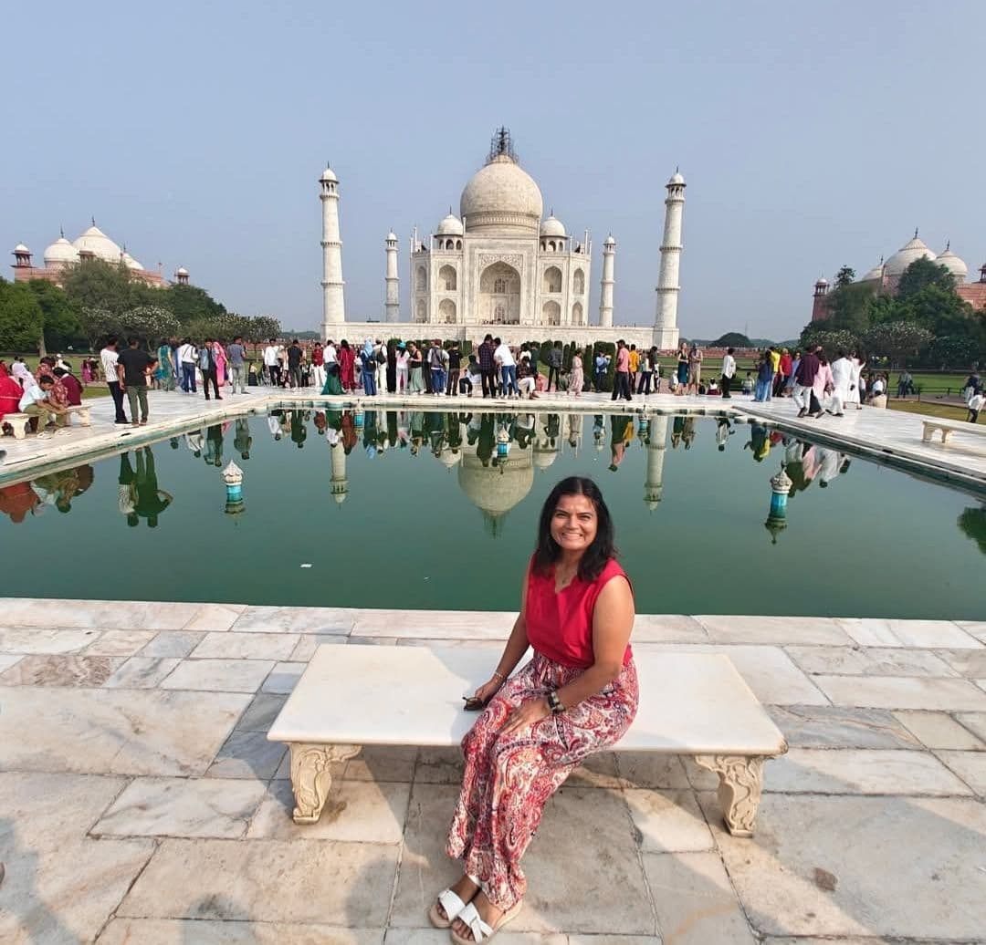 Taj Mahal reflected in a long pool with a woman sitting on a marble bench in front, Agra, India.