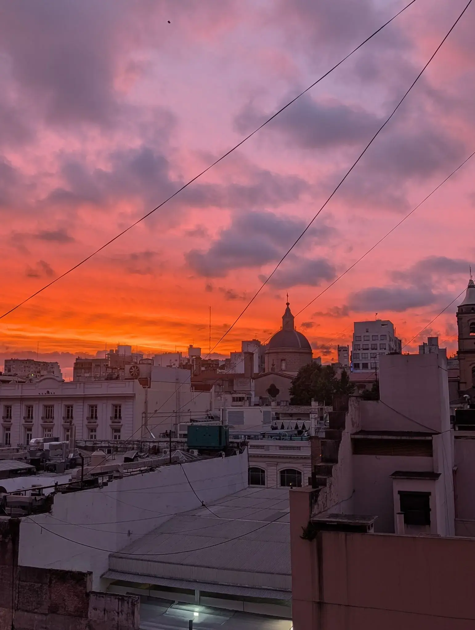 Pink-orange sunset over downtown Buenos Aires, Argentina, with rooftops and a church dome silhouetted.