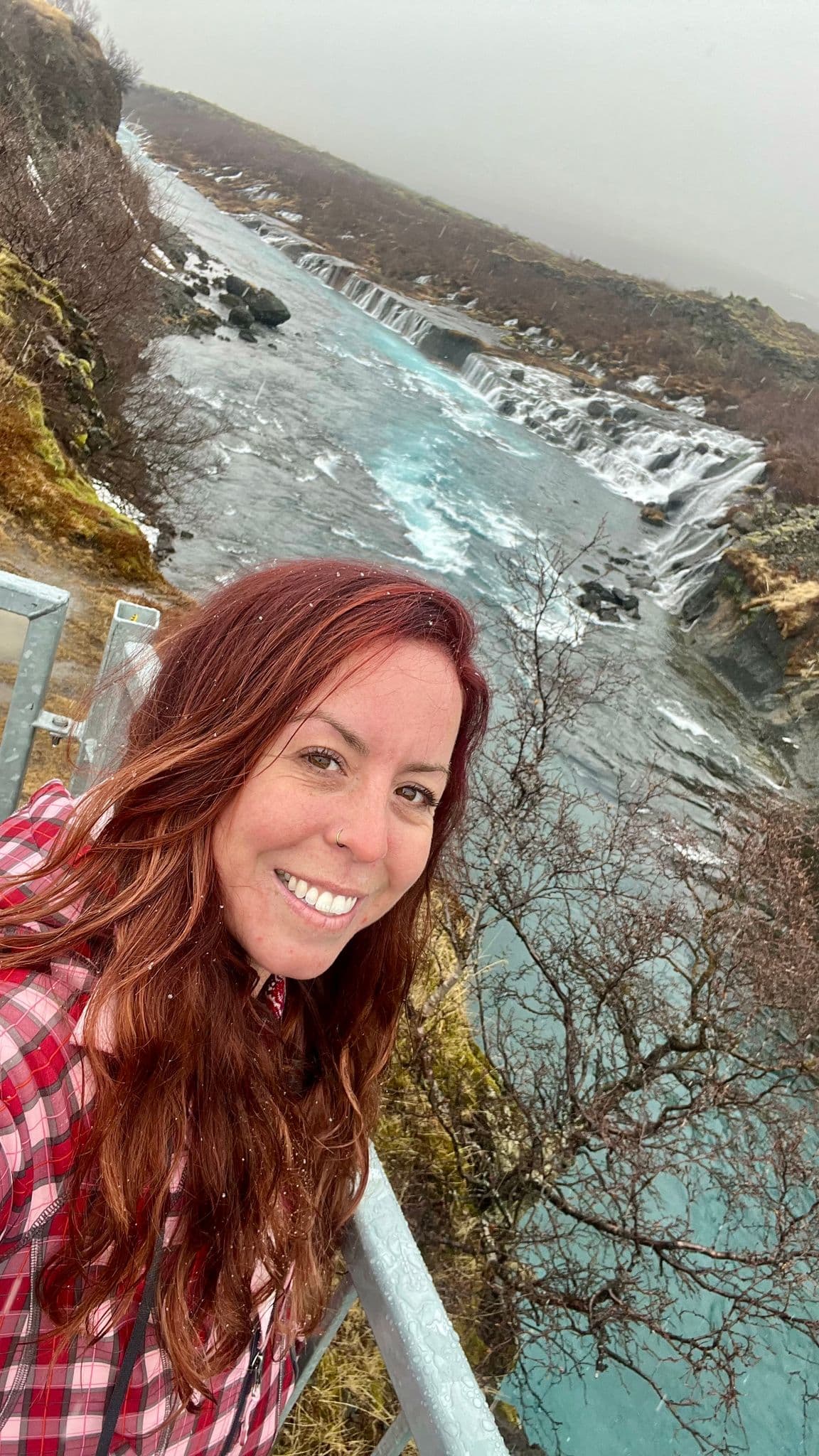 Turquoise river with small cascades and a woman taking a selfie from a bridge in a rocky Iceland landscape, Iceland.