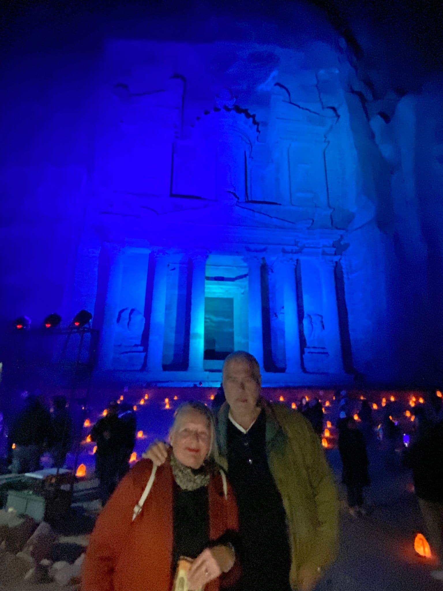 Al-Khazneh (The Treasury) at Petra lit blue at night with two travelers posing in front during a tour in Petra, Jordan.