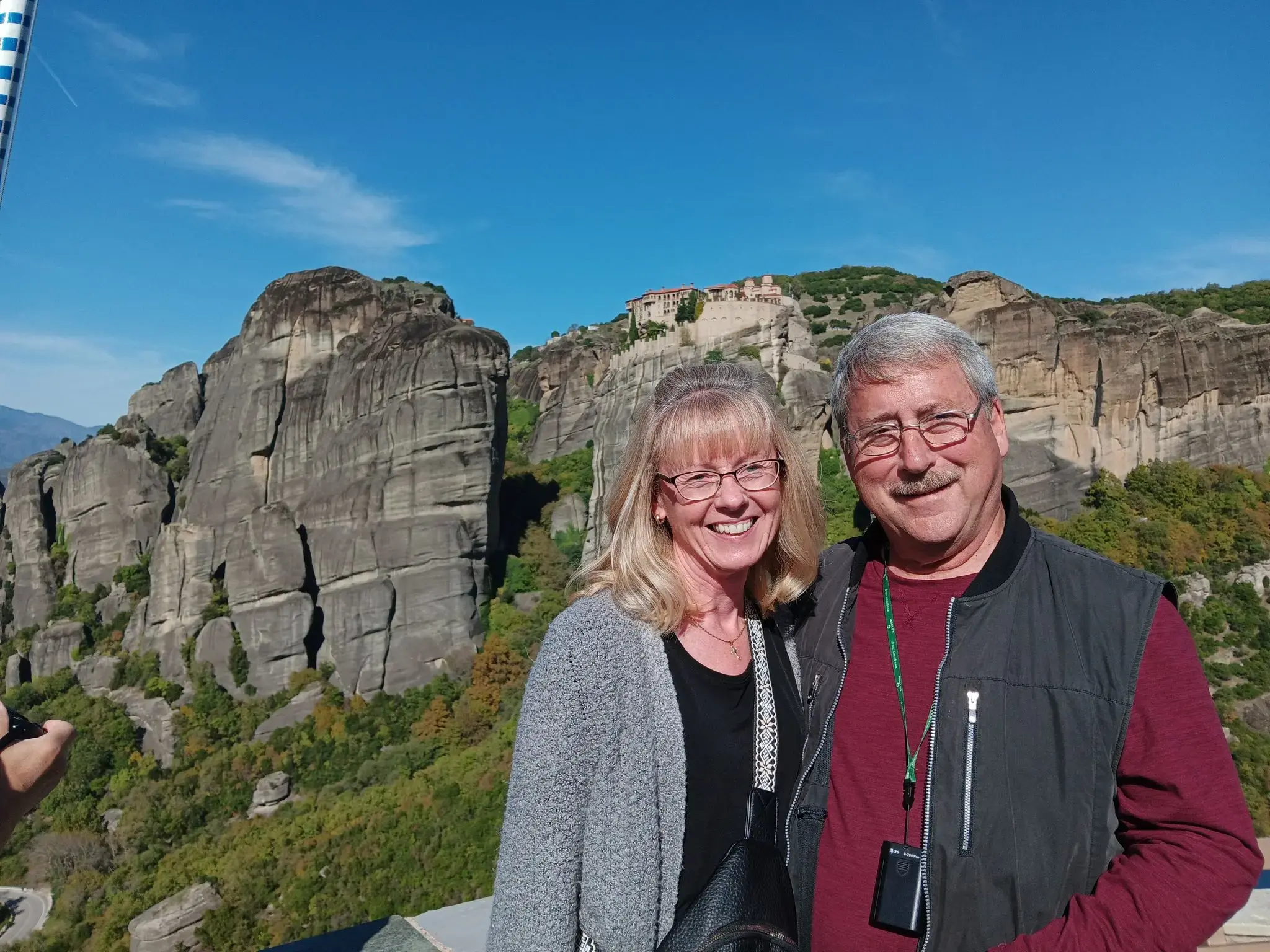Meteora rock cliffs and cliffside monastery with a smiling couple posing on a viewpoint, Meteora, Greece.