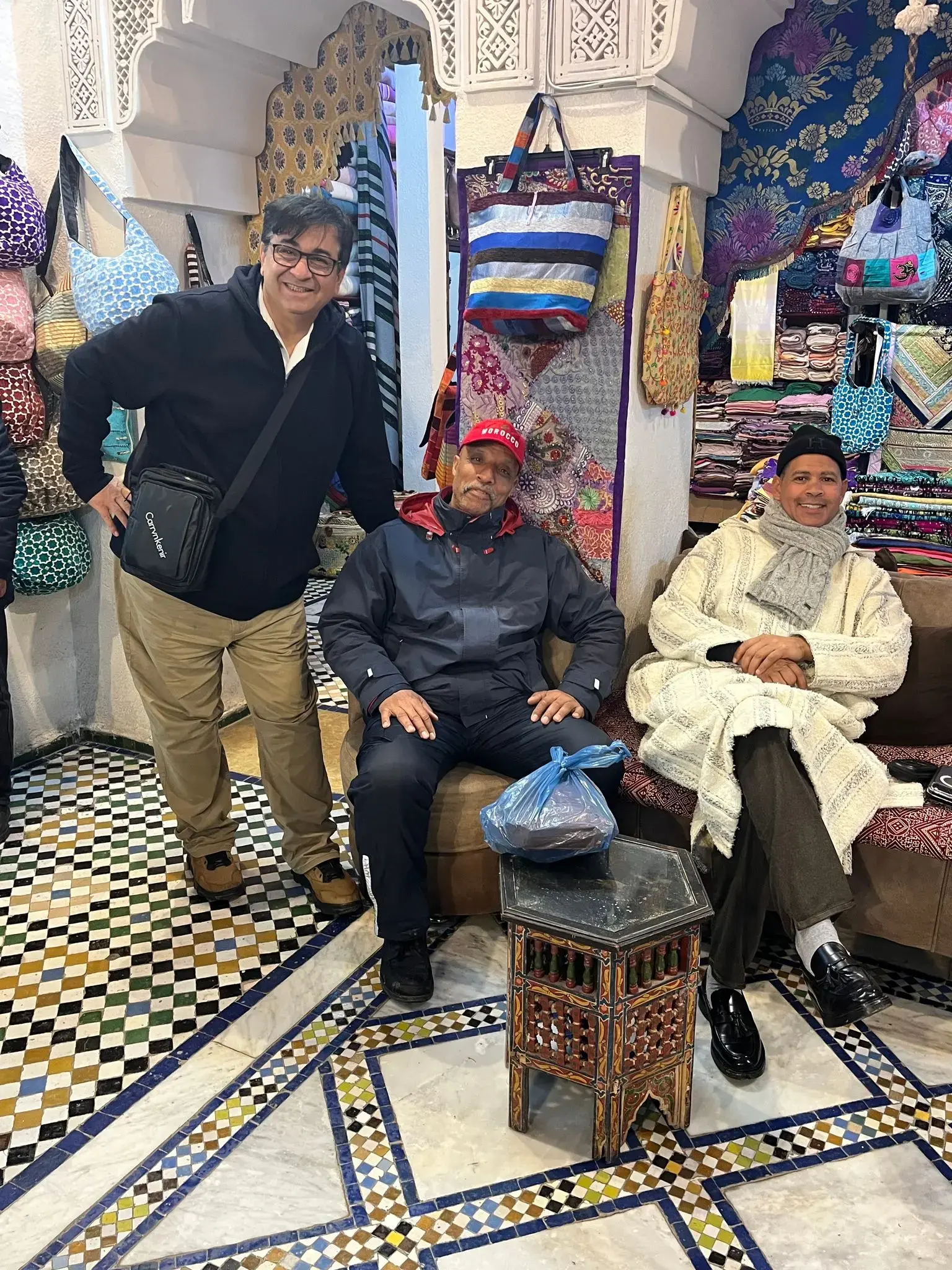 Three men sitting in a colorful textile stall in the Fez medina bazaar, Fes, Morocco.