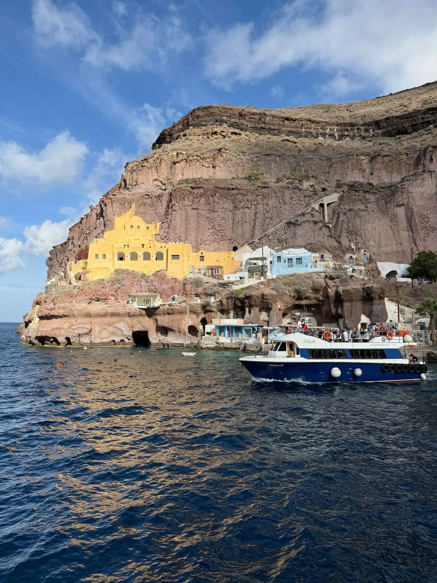 Cliffside buildings at Ammoudi Bay, Oia with a small tour boat on the Aegean Sea, Santorini, Greece.
