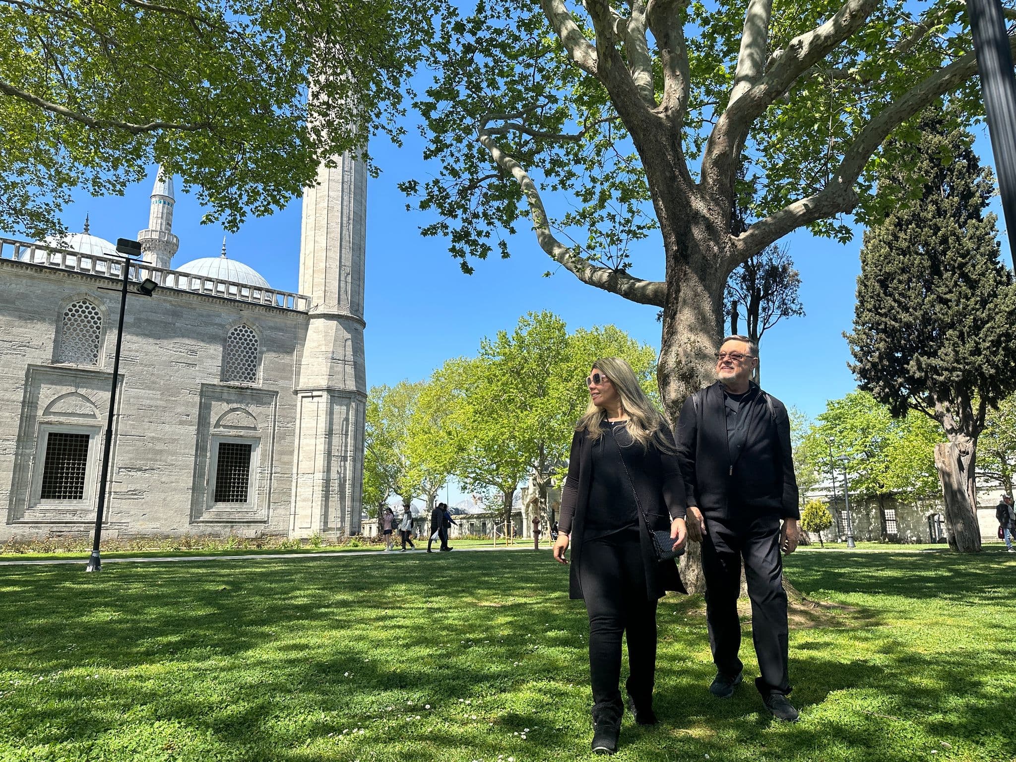 Süleymaniye Mosque domes and minaret with two people walking on a grassy lawn in Istanbul, Turkey.