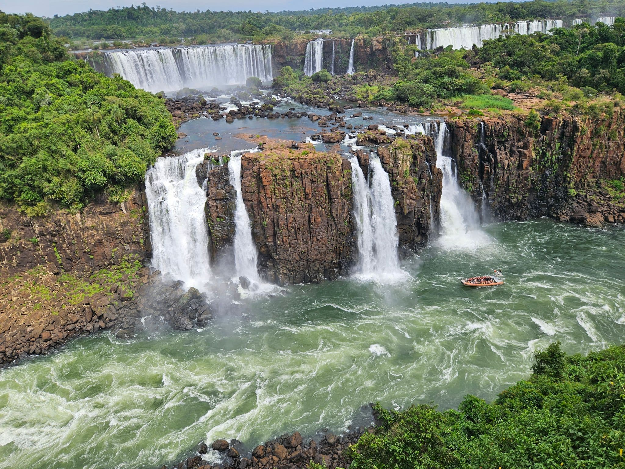 Iguazu Falls with multiple cascades plunging over cliffs and a small tour boat in the river, Foz do Iguaçu, Brazil.