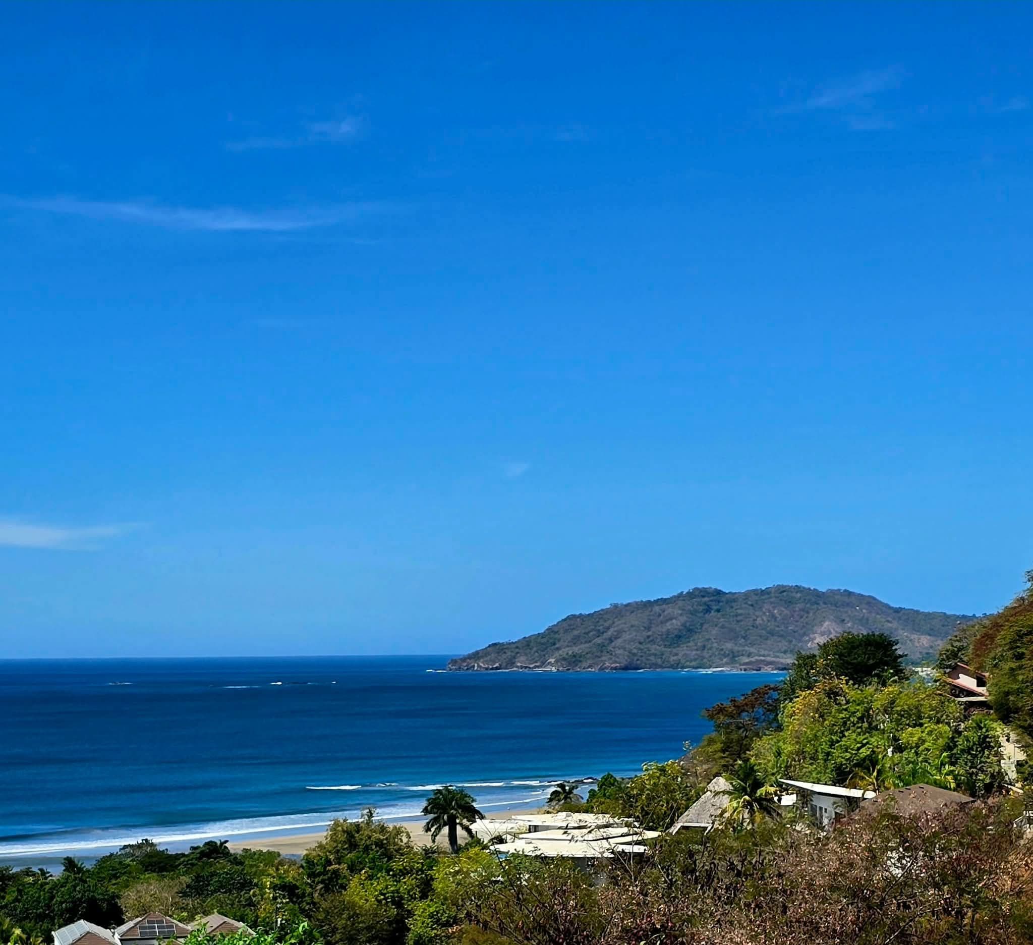 Tamarindo Beach coastline with blue Pacific waters, sandy shore and a tree-covered headland in Guanacaste, Costa Rica.