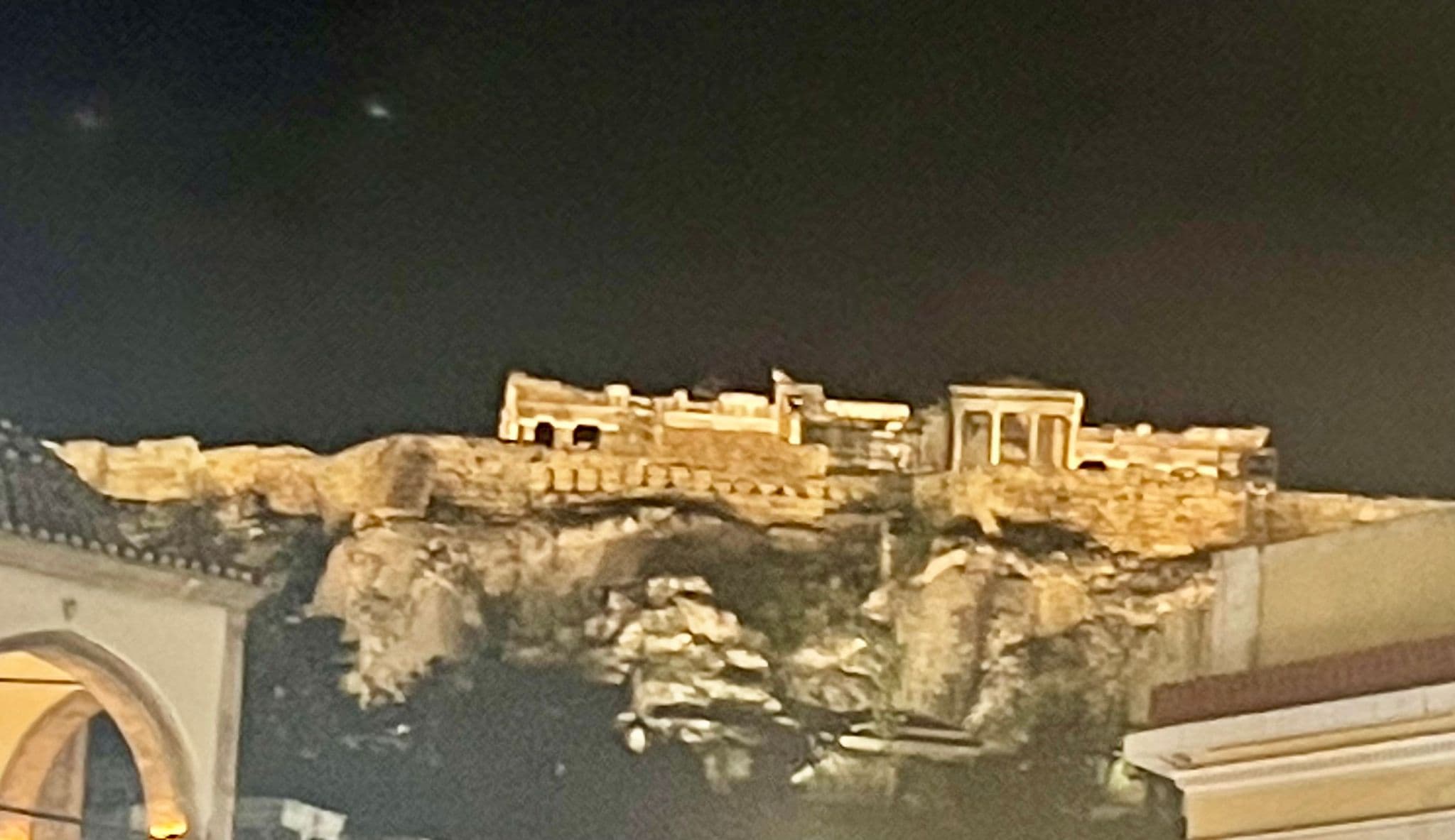 Acropolis of Athens lit at night with ancient temple ruins on a rocky outcrop, viewed from near the Agora, Greece.