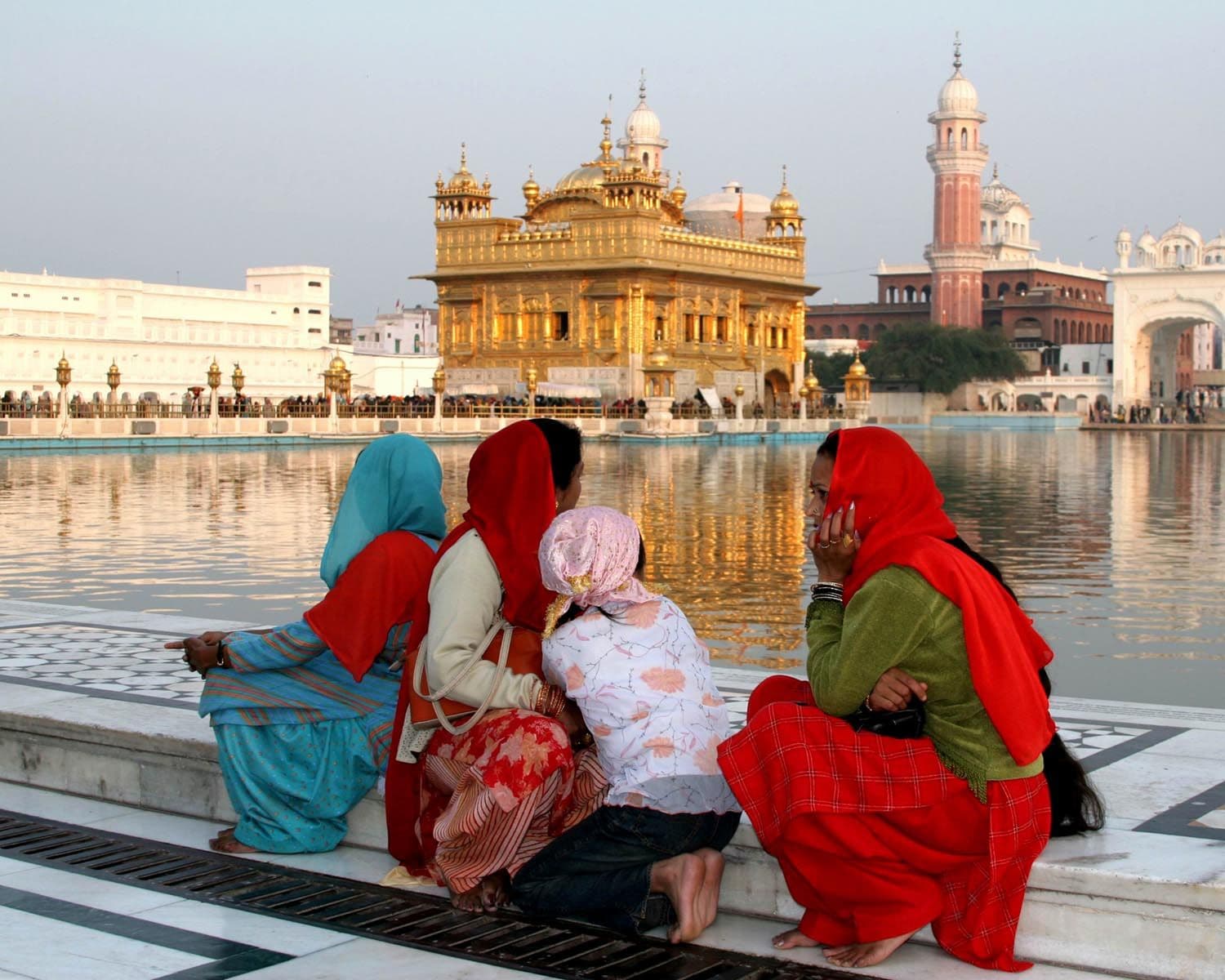 Golden Temple (Harmandir Sahib) reflecting in the sarovar as a family sits on the marble edge in Amritsar, India.