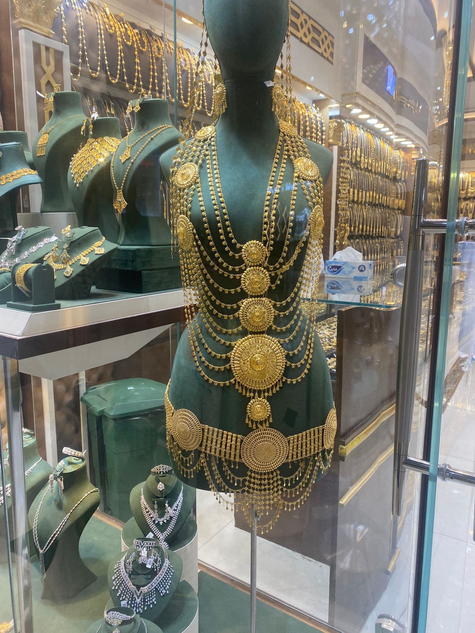 Layered ornate gold body jewelry draped on a mannequin inside a jewelry shop window.