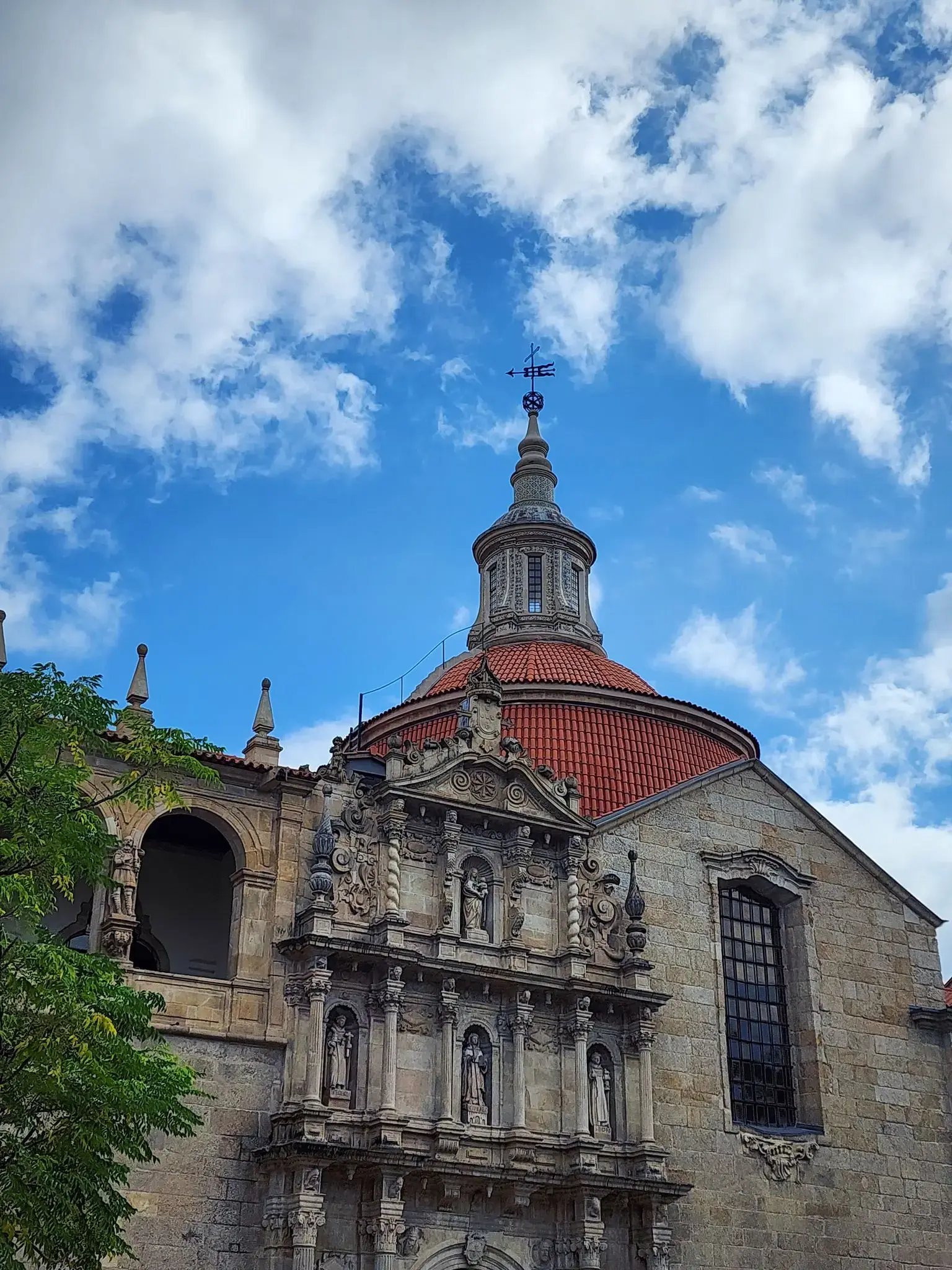 Ornate stone church facade with a red-tiled dome against a bright blue sky in Portugal.